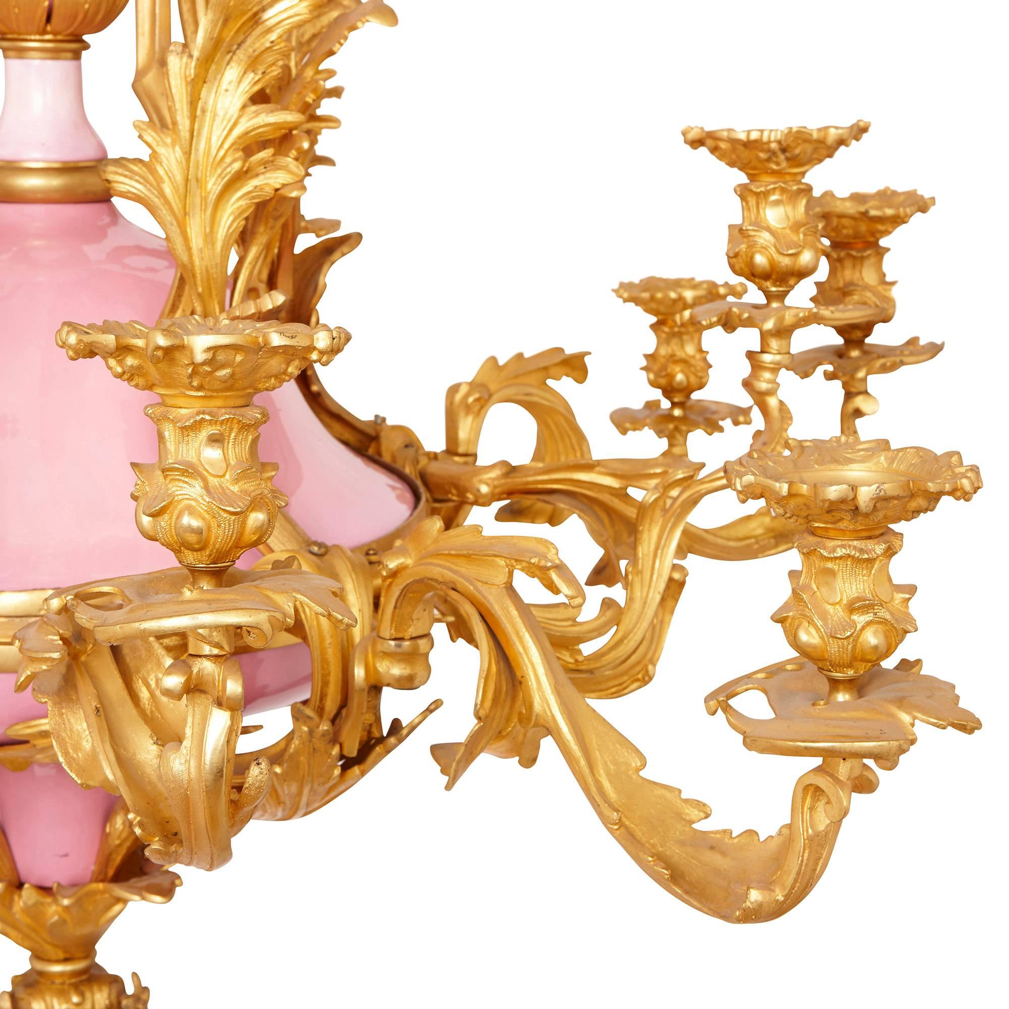 This beautiful antique French chandelier is crafted in the elegant Belle Époque style. The chandelier features a delicate pink porcelain body, which is offset by the surrounding golden gilt bronze to create a vivid visual contrast. Issuing from the