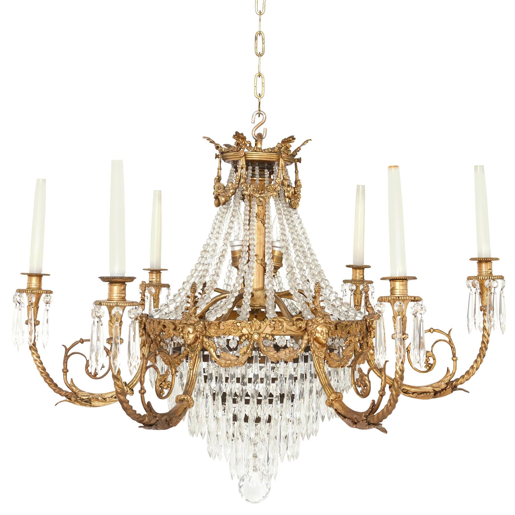 This elegant French antique Empire style chandelier is crafted in the refined Empire style, featuring a central structure of gilt bronze that issues scrolling branches for lights. The chandelier is adorned with finely cut-glass beads and droplets,