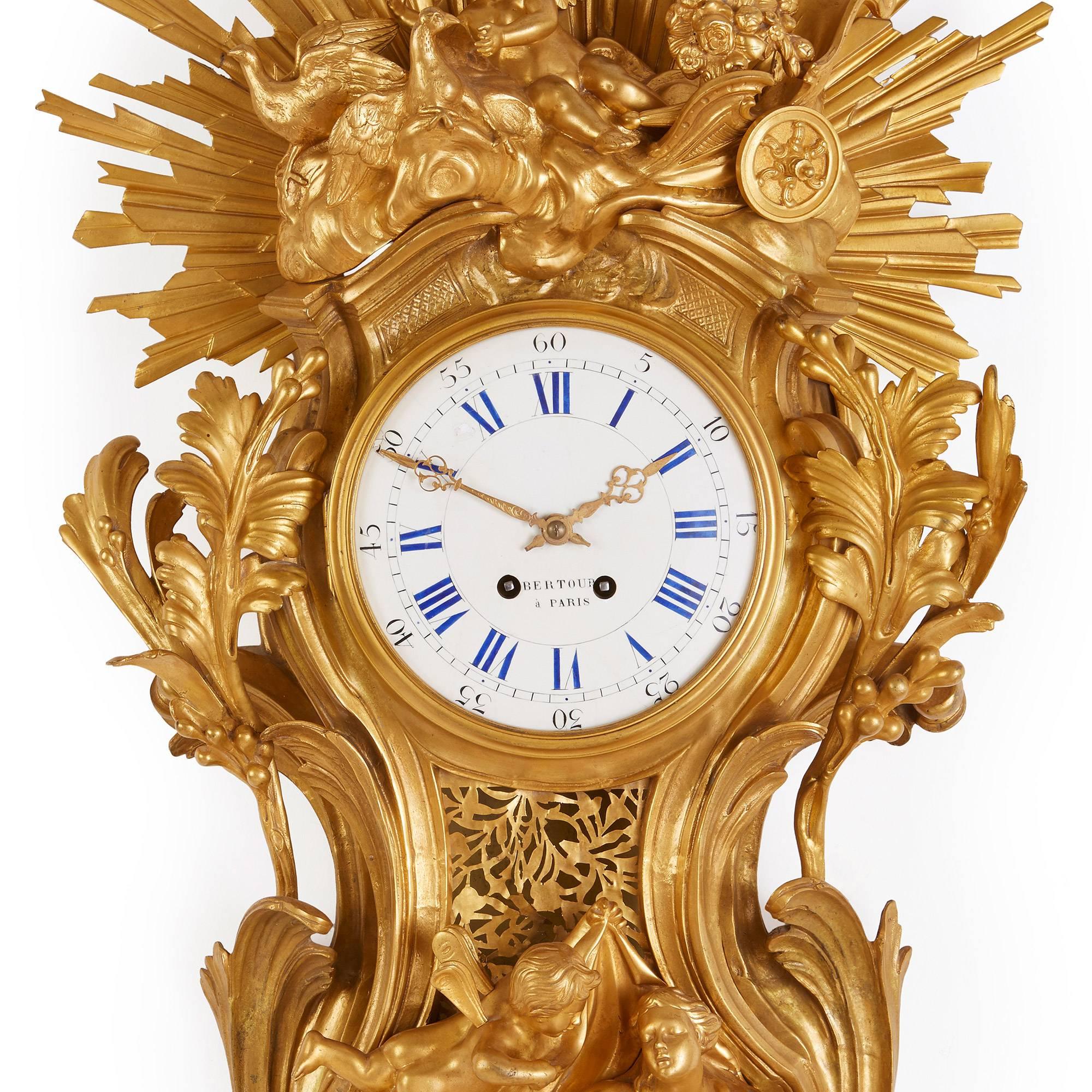 This beautiful Belle Époque style Cartel clock is notable for its stunning depiction of a sunburst, which is depicted in vivid golden gilt bronze. The central circular enamel dial is set within an elaborately detailed ormolu case depicting multiple