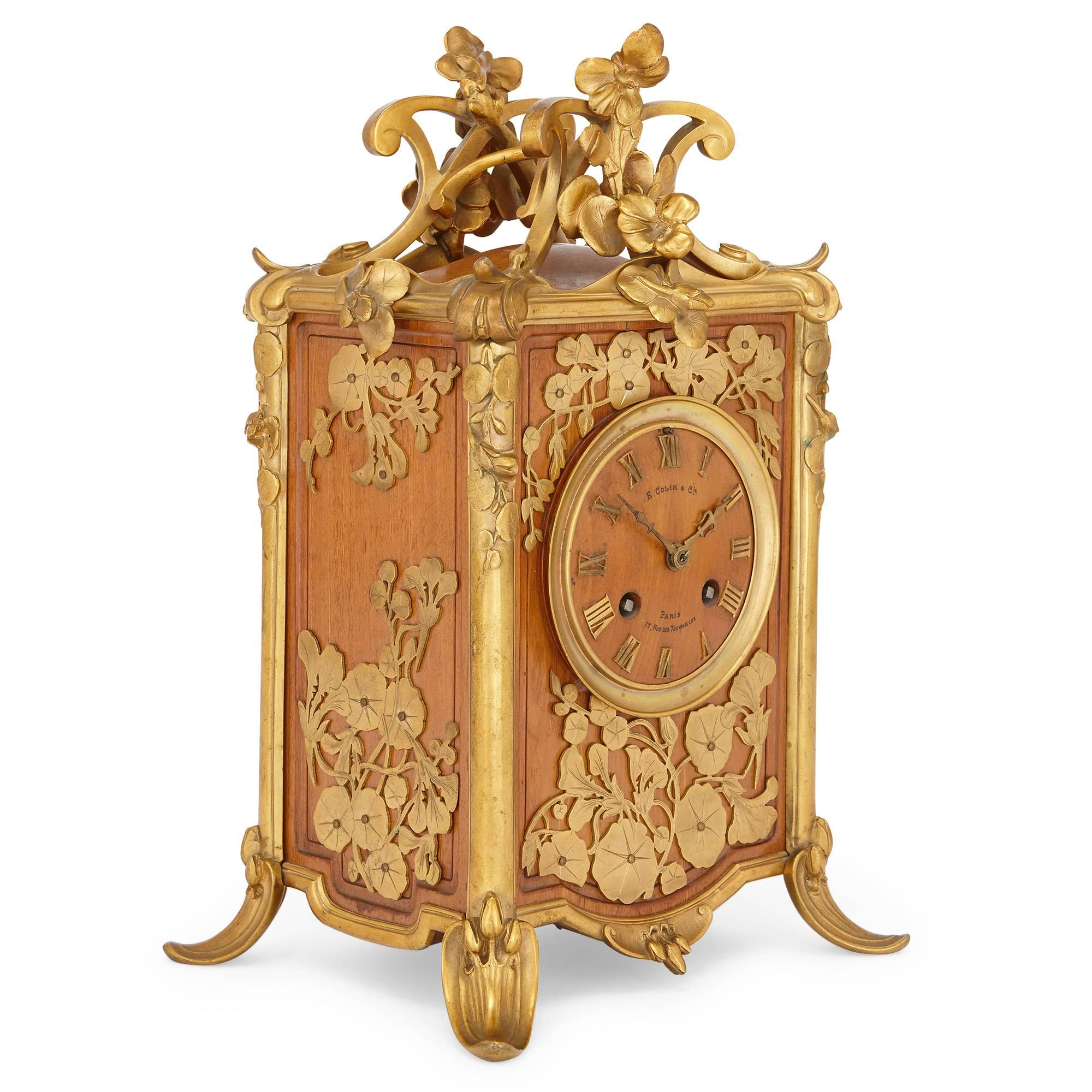 Cette élégante horloge de cheminée ancienne, de la période de l'Art nouveau, est placée dans un beau coffret rectangulaire en bois, orné de bordures en bronze doré (ormolu) et de décorations florales.

La pendule a été fabriquée par le célèbre