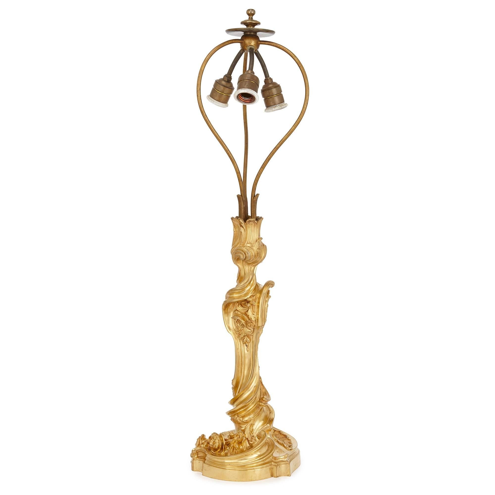 Rendered in the flamboyant Rococo style, this charming antique table lamp would make a beautiful addition to any elegant interior. Featuring a twisted gilt bronze base with scrolling, asymmetric detailing, the lamp is of Classical form and in the