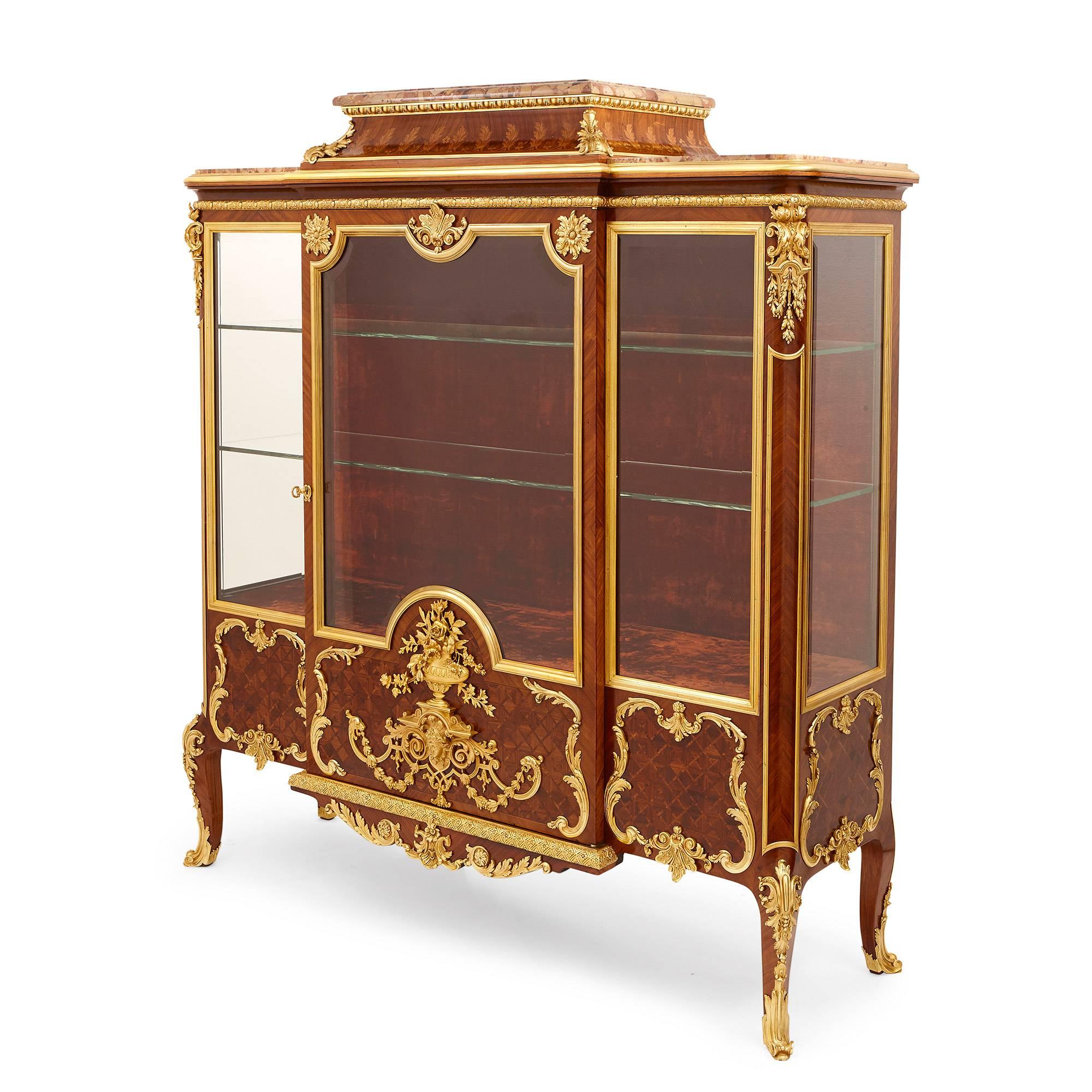 This fine antique vitrine is attributed to the famous French maker, Grimard, on account of its high quality materials and exquisite craftsmanship. 

The vitrine features three stepped marble tops, with the central top above a frieze of marquetry