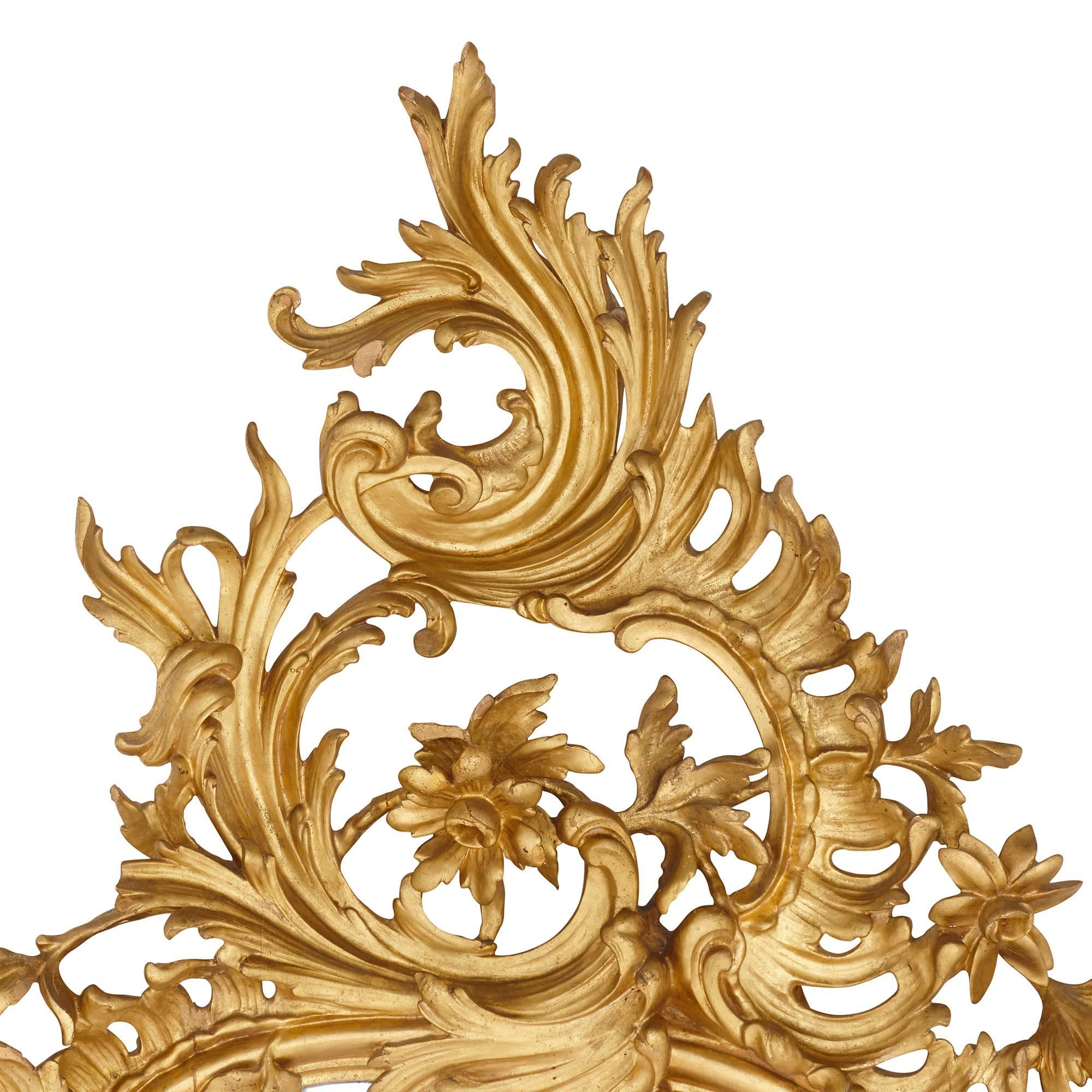Cet exceptionnel miroir ancien de style rococo est sculpté dans du bois doré. Le style rococo a été relancé au XIXe siècle et ce miroir en présente les principales caractéristiques dans son cadre orné, qui a été magistralement façonné en motifs