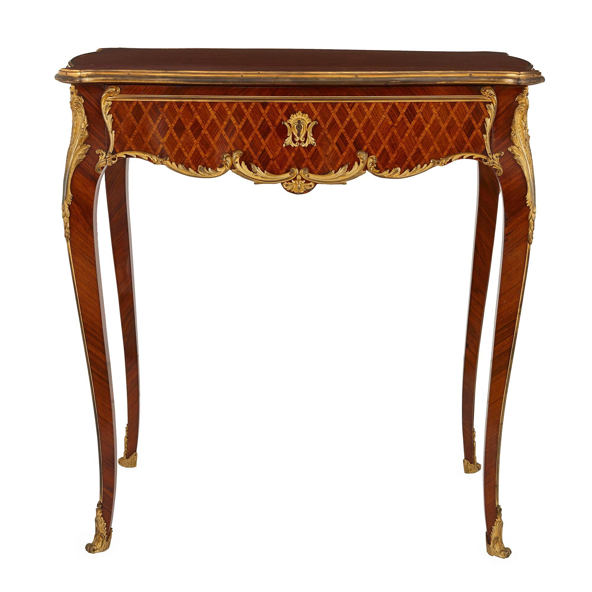 This late 19th century Louis XV style French side table features an intricate parquetry design in a diamond-shape pattern. The top and skirting of the table both feature this design and are bordered with scrolling acanthus leaf gilt bronze mounts