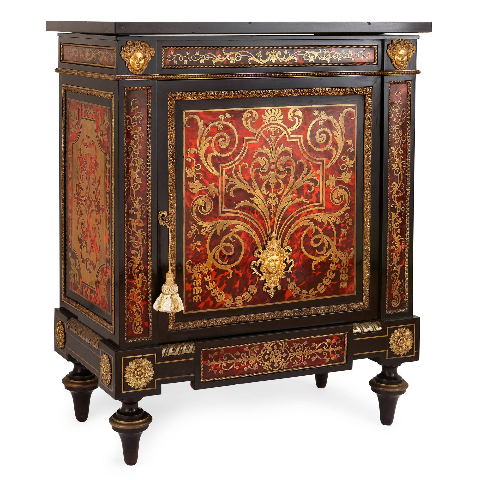 This antique French cabinet features intricate Boulle-style brass and tortoiseshell marquetry and is mounted with fine ormolu decorations. It is built from ebonized wood, takes a rectangular shape and is set on four cylindrical feet. The base of the