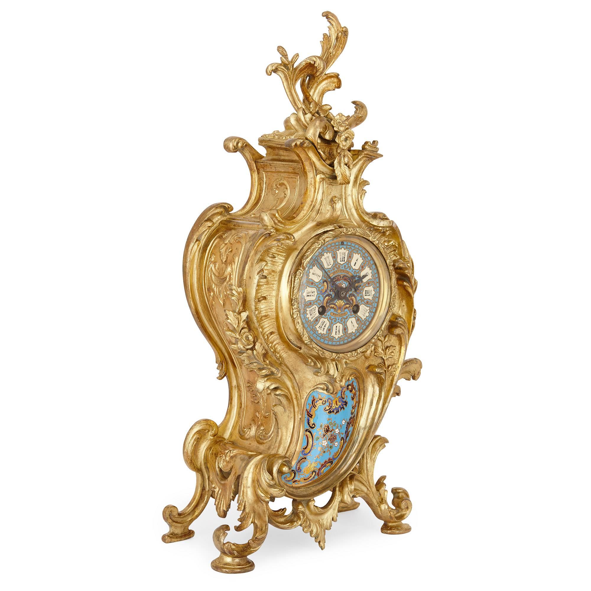 This playful, decorative clock set is made up of three pieces, which include a central clock and a pair of flanking candelabra. The central clock is cast in ormolu, shaped asymmetrically and decorated all over with Rococo style scrolls and acanthus