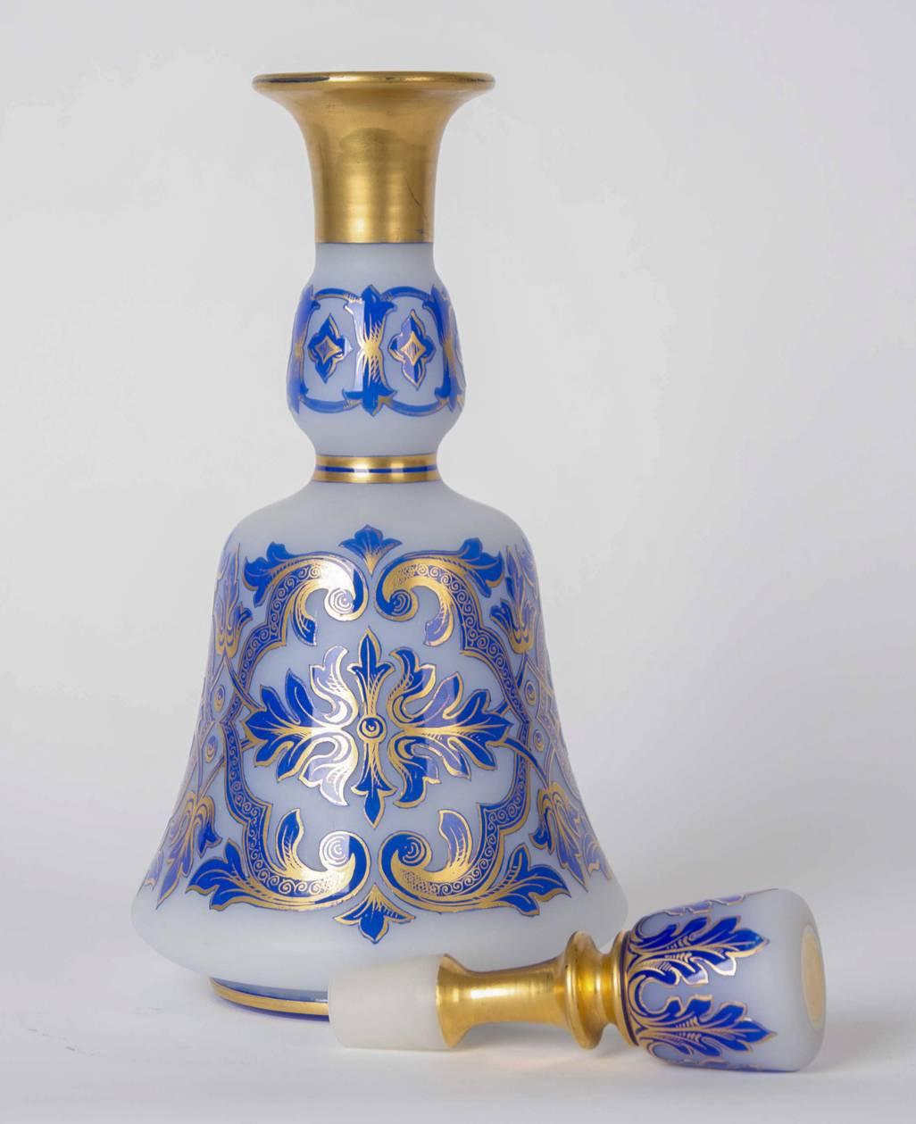 This antique luxury drinking set dates from the late 19th Century and consists of four pieces: a decanter with a stopper, a bon-bon jar with a cover and two goblets. The goblets have gilt stems and rims and feature a foliate blue glass overlay