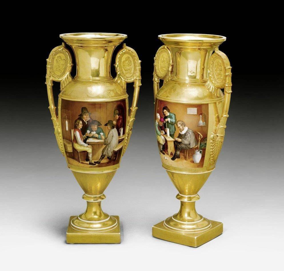 This pair of antique porcelain vases, dating from the early 19th century in the period of Napoleonic rule known as the Empire period, are decorated with rich gilt ground and feature Fine cartouches on the front and reverse. The vases are set on