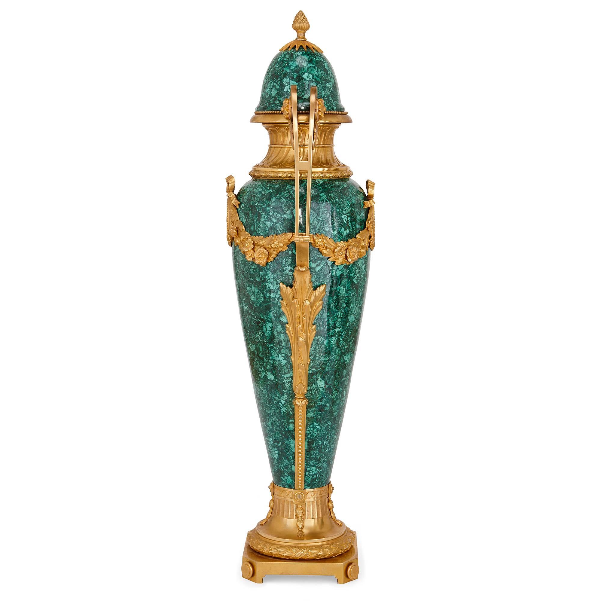 These elegant Neoclassical style vases take a tall, slender ovoid shape, and make an impressive statement in their combination of rich, intense green malachite and luxurious gilt bronze. They are set on square ormolu bases and supported by circular