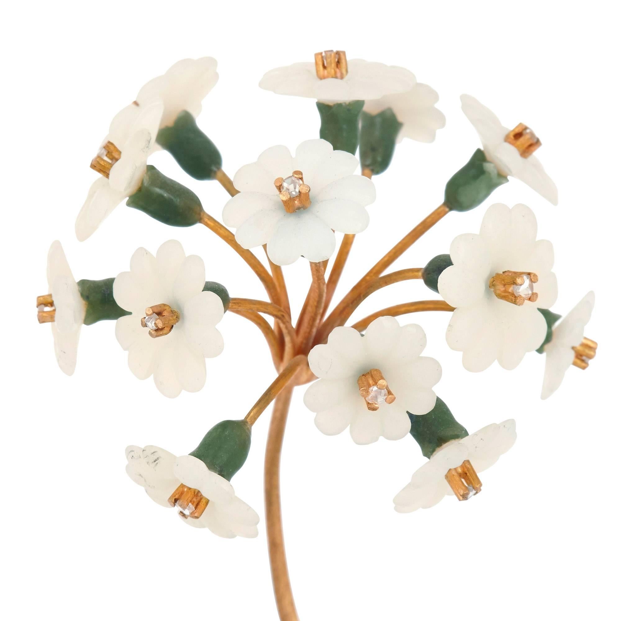 This delicate flower model is exquisitely crafted from the finest materials. The model features a cluster of small white, hardstone flowers, with diamond stigmata, set onto a central gold stem with leaves formed of green nephrite. The flower stands