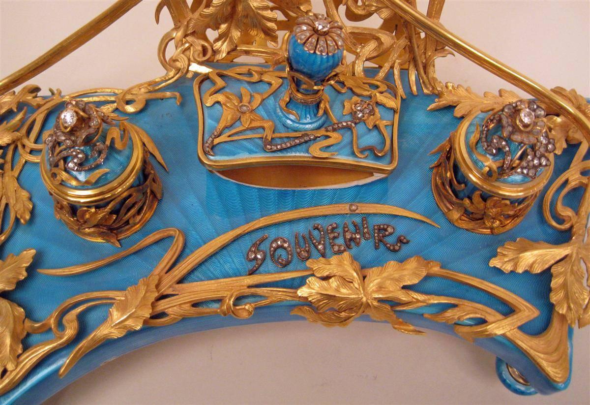 Questo raffinato set da scrivania russo è caratterizzato da scintillanti diamanti rosa e argento dorato. Il set comprende un francobollo, due calamai, un portalettere e una cornice, tutti posizionati su un supporto. Il supporto è rivestito di smalto