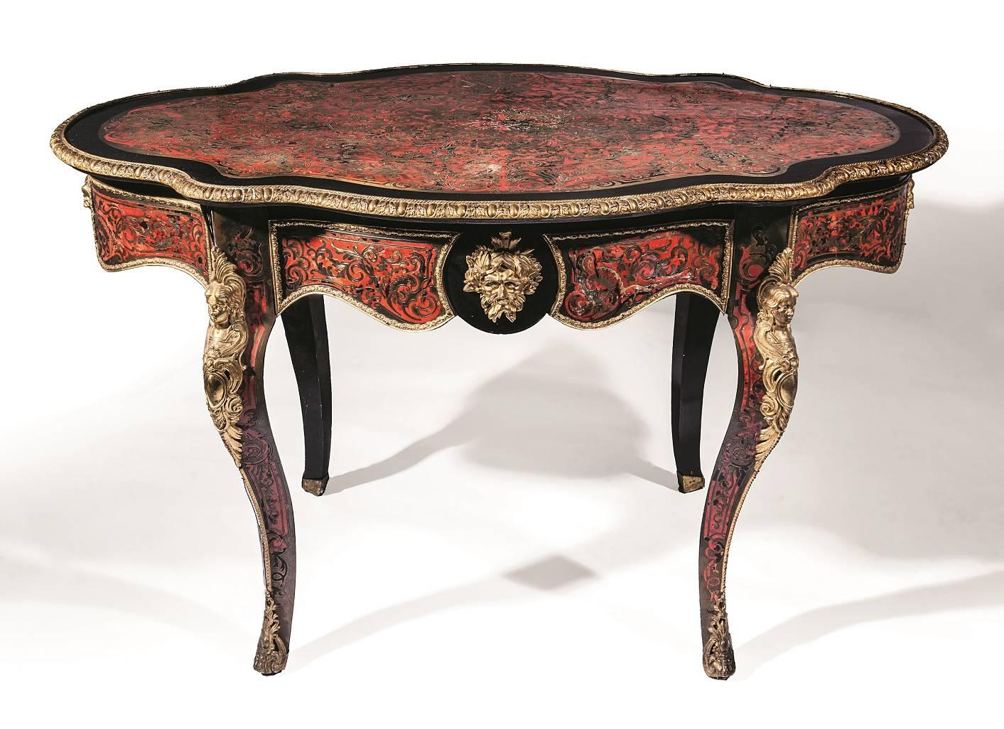 This fine table is crafted in ebonised wood and features gilt bronze mounts and Boulle style marquetry. The table is of curved, oval shape, and is inlaid with marquetry to the top, around the edges and along the lengths of the legs. The legs are of