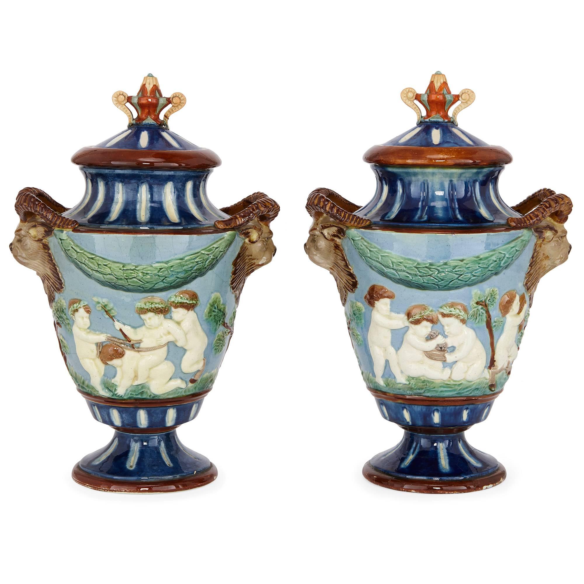 This fantastic pair of antique ceramic vases have a sculptural quality: decorated in relief on the exterior of their bodies with scenes of putti (Cupid figures) playing in a landscape setting with light blue ground. Each vase features twin handles