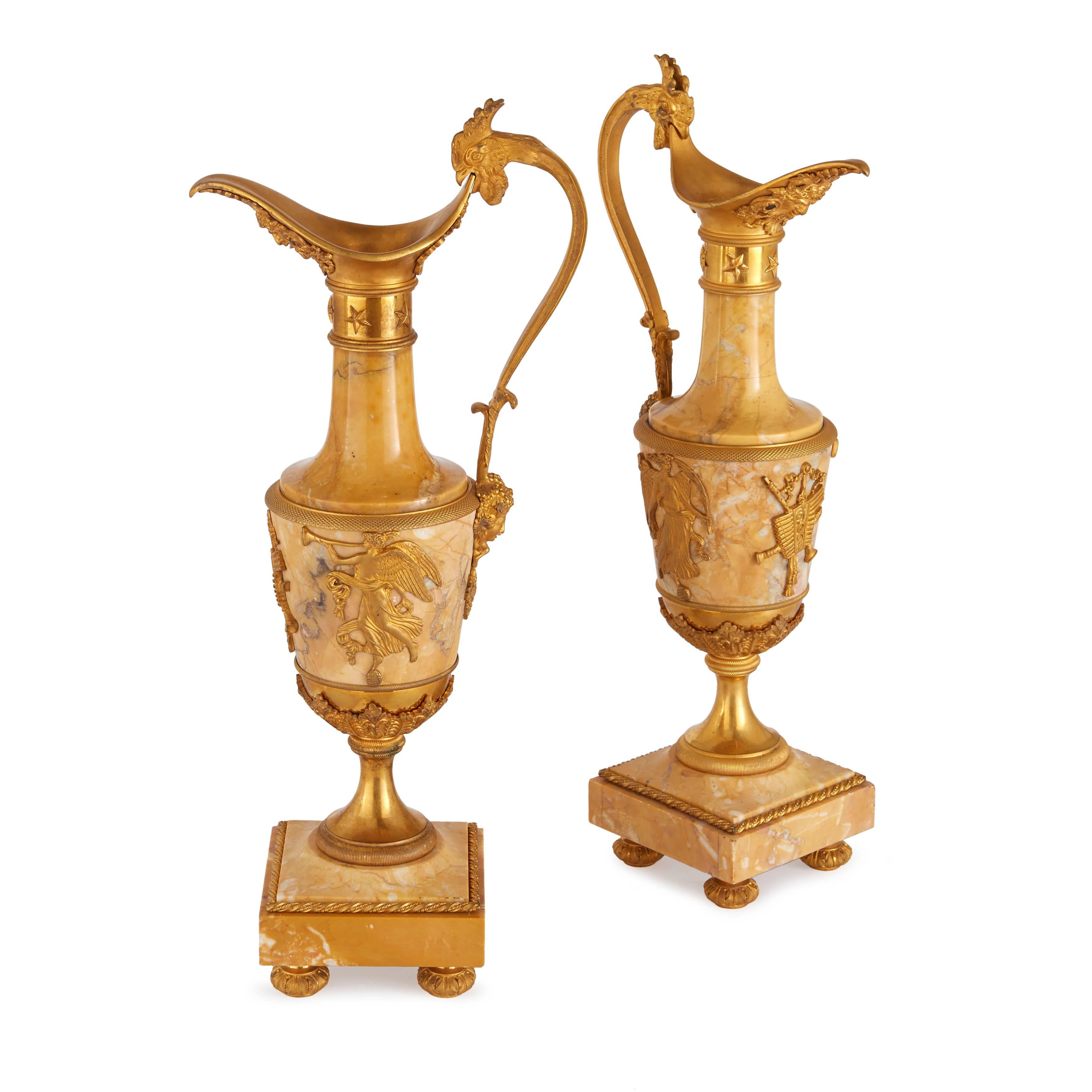 In the form of Amphora ewers, each ornately mounted with masks by the spout, handle in the form of a rooster at the top, with a mask at the end, the body appliqued with allegories of music, on a square base with ormolu mounted feet.