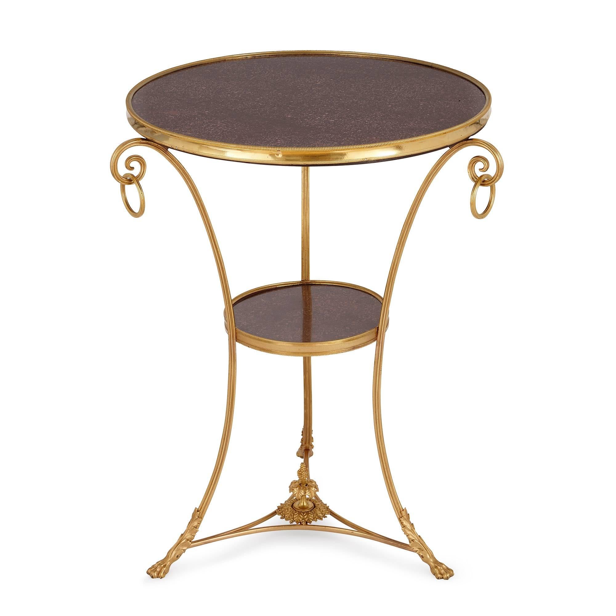 The circular porphyry top with ormolu band, on three curved legs joined by a small circular porphyry shelf in the middle, ending in paw feet.

The beauty of this circular gueridon is in its refined simplicity of design, allowing the highly prized