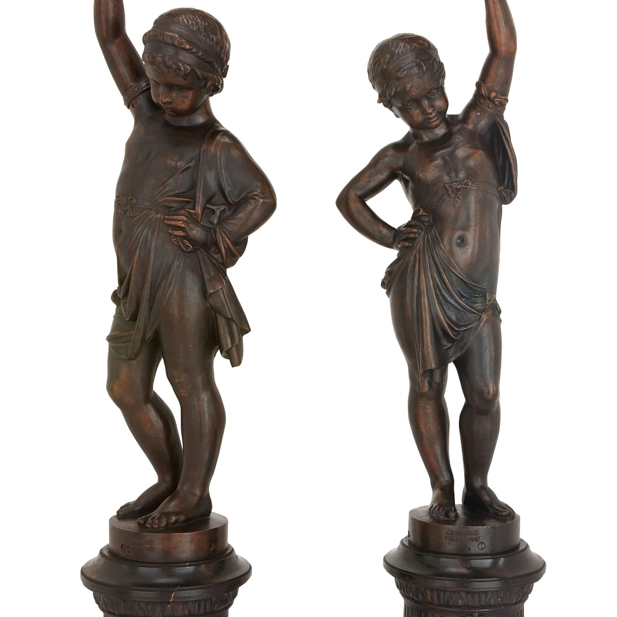 Each depicting a young male figure holding aloft a torch, on a pair of faux marble pedestals decorated with masks.

The company of A. Durenne, maître de forges, was established in 1847 by Antoine Durenne at Sommevoire. Their catalogues of 1877 and