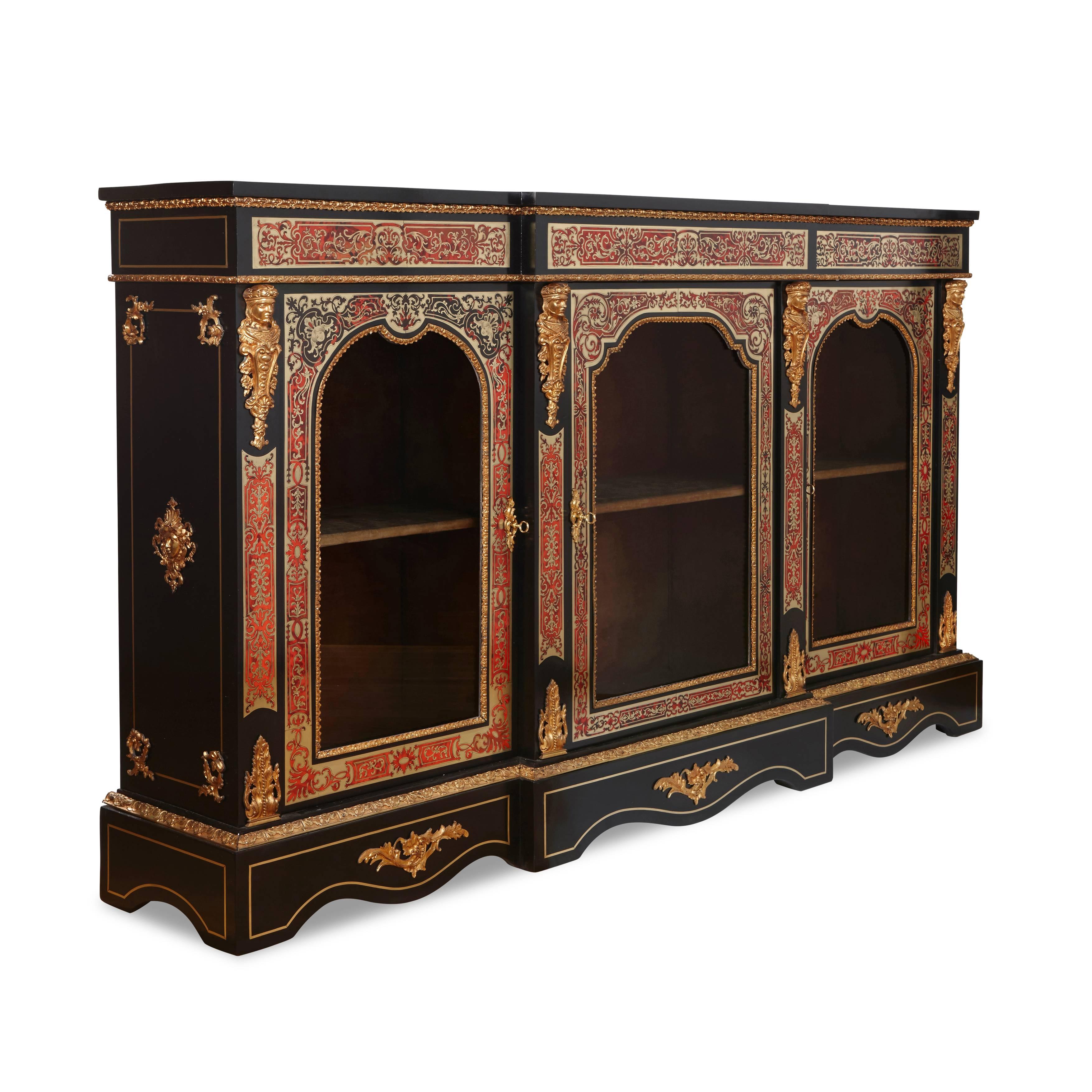 With inlaid Boulle work panels of inlaid brass and tortoiseshell, applied with four classical caryatid ormolu mounts in between three glazed arch panel doors enclosing a velvet lined shelved interior, the reverse of the central door with brass label