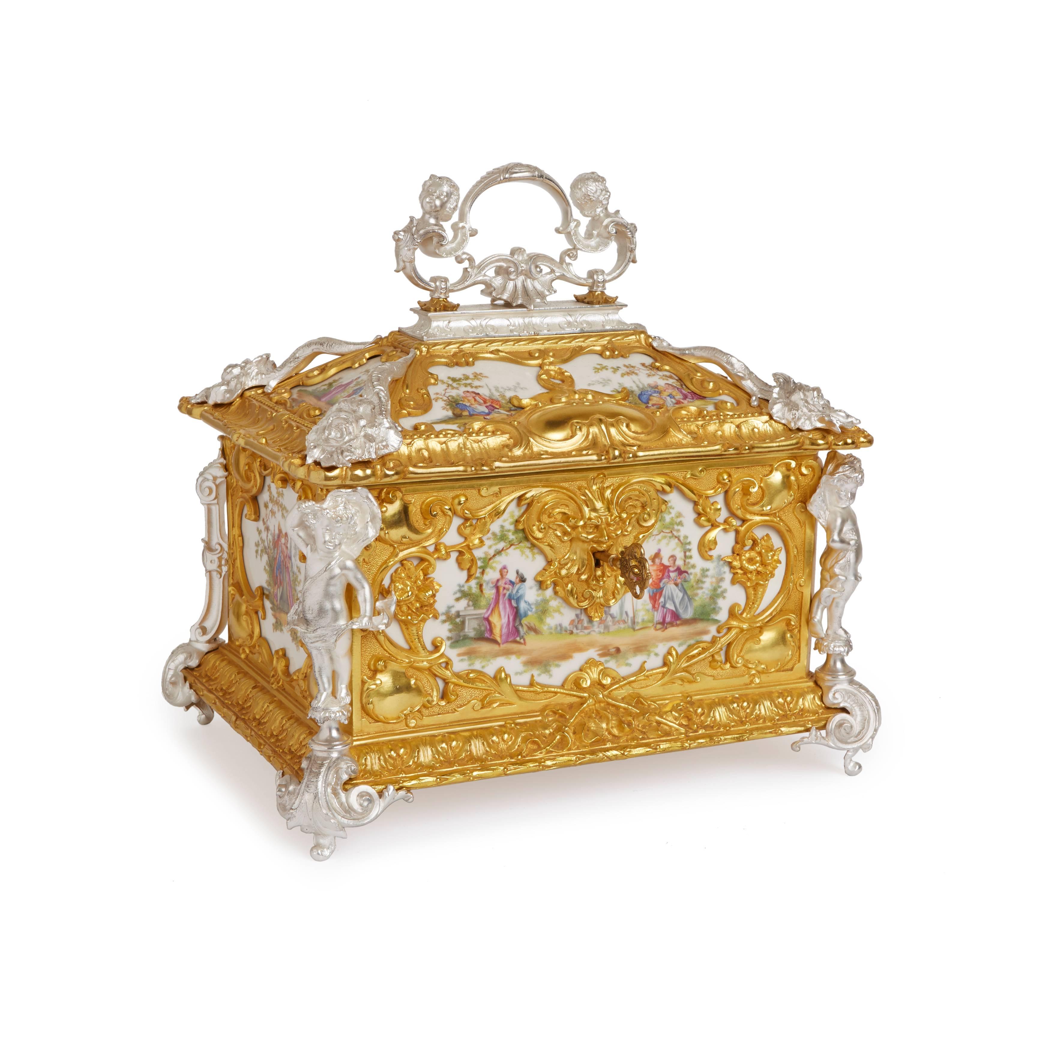 Of rectangular form, the porcelain plaques depicting amorous couples mounted with rich gilt and silvered bronze corner mounts with scrolls, cornucopias, bows, and a grotesque mask escutcheon, the hinged cover topped with a silvered bronze cherub
