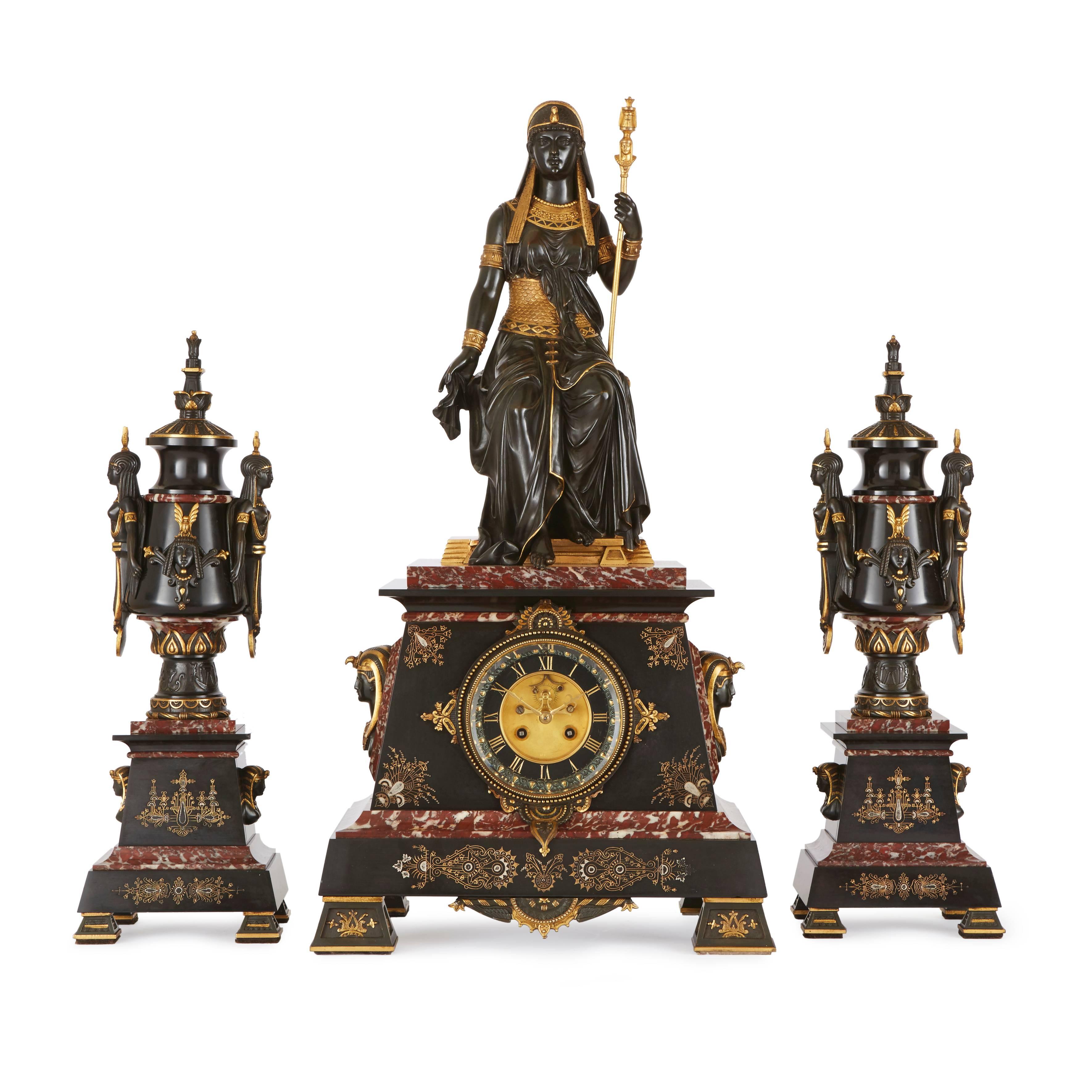 Attributed to Emile Herbert, French, 1828-1893.
Comprising a central clock and a pair of flanking lidded vases, the clock on a red and black marble base with Pharaoh busts on either side, surmounted with the Egyptian queen 'Isis' enthroned, the two