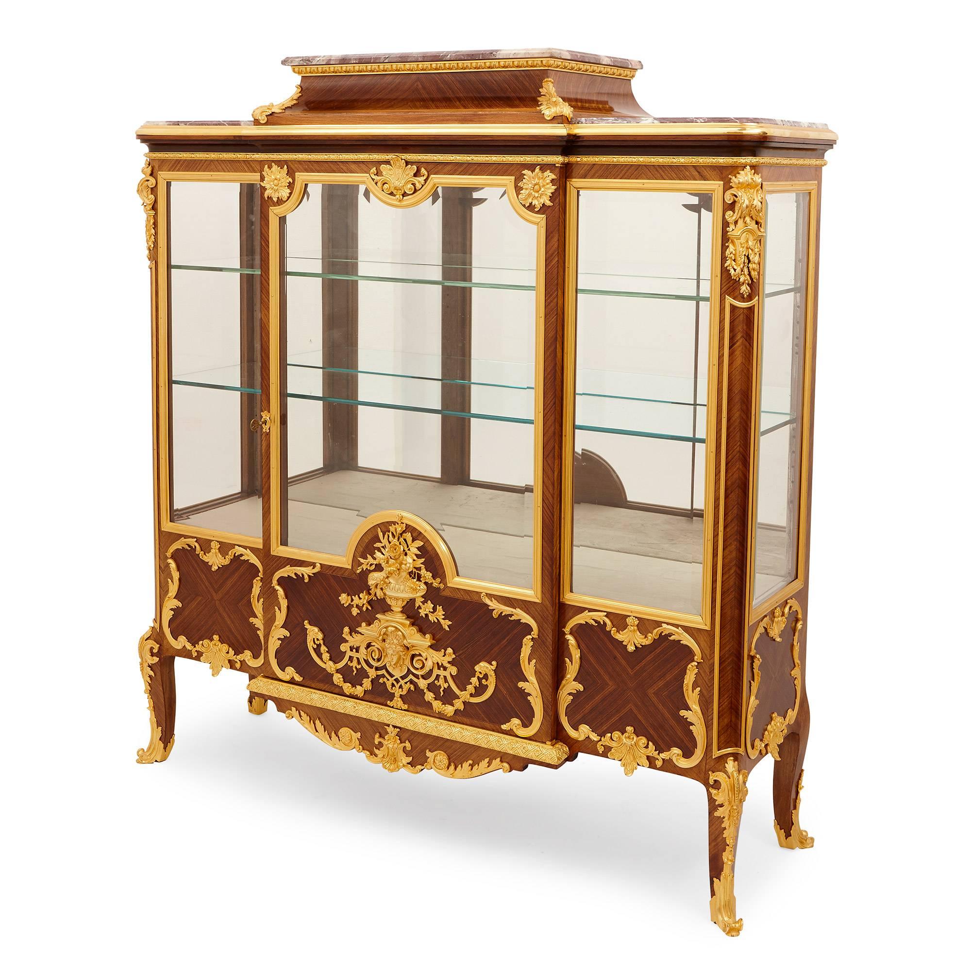 The cartouched door frame mounted with acanthus and ornate floral motifs enclosing two glass shelves and a mirrored back flanked by two smaller glaze panels, ormolu casts and a cartouche frame mounted below, with shaped cabriole legs on ormolu