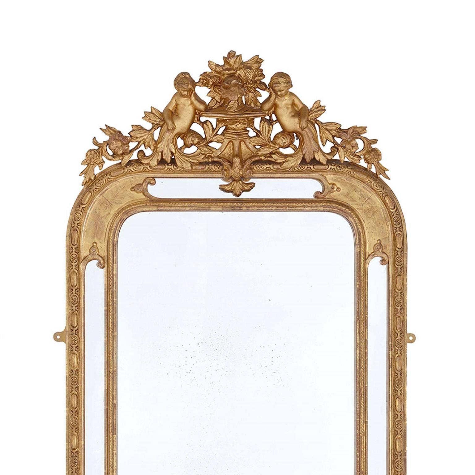 This pair of French mirrors are carved in the elegant neoclassical style. Each mirror is formed of a rectangular carved giltwood frame with curved edges at the top. Surmounting each frame is a vase with flowers flanked by two putti. Foliate