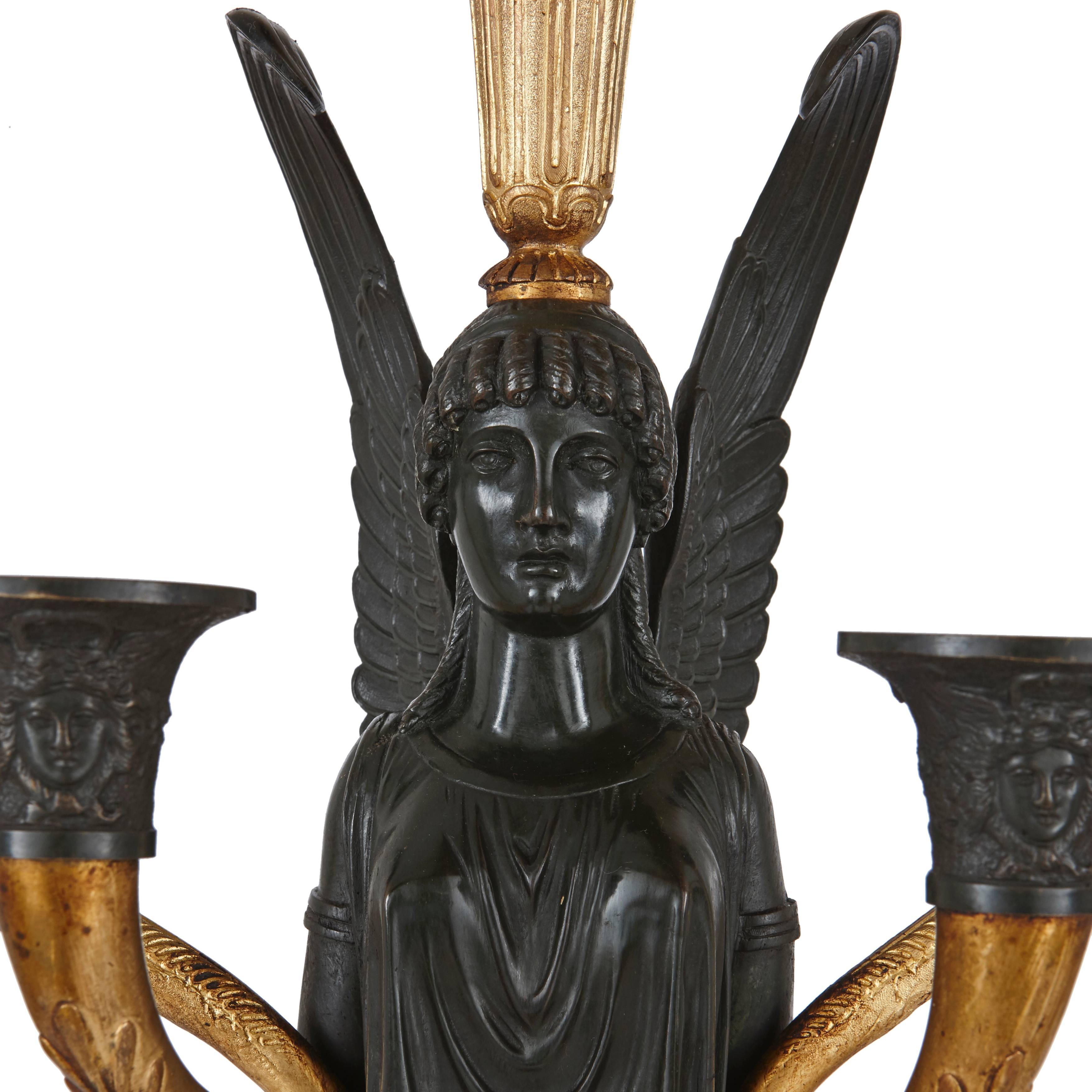 A pair of Empire gilt and patinated bronze candelabra. Each with a winged Victorian female figure carrying a torchère on their head and light arms to the side with a square shaped Giallo di Siena marble base.