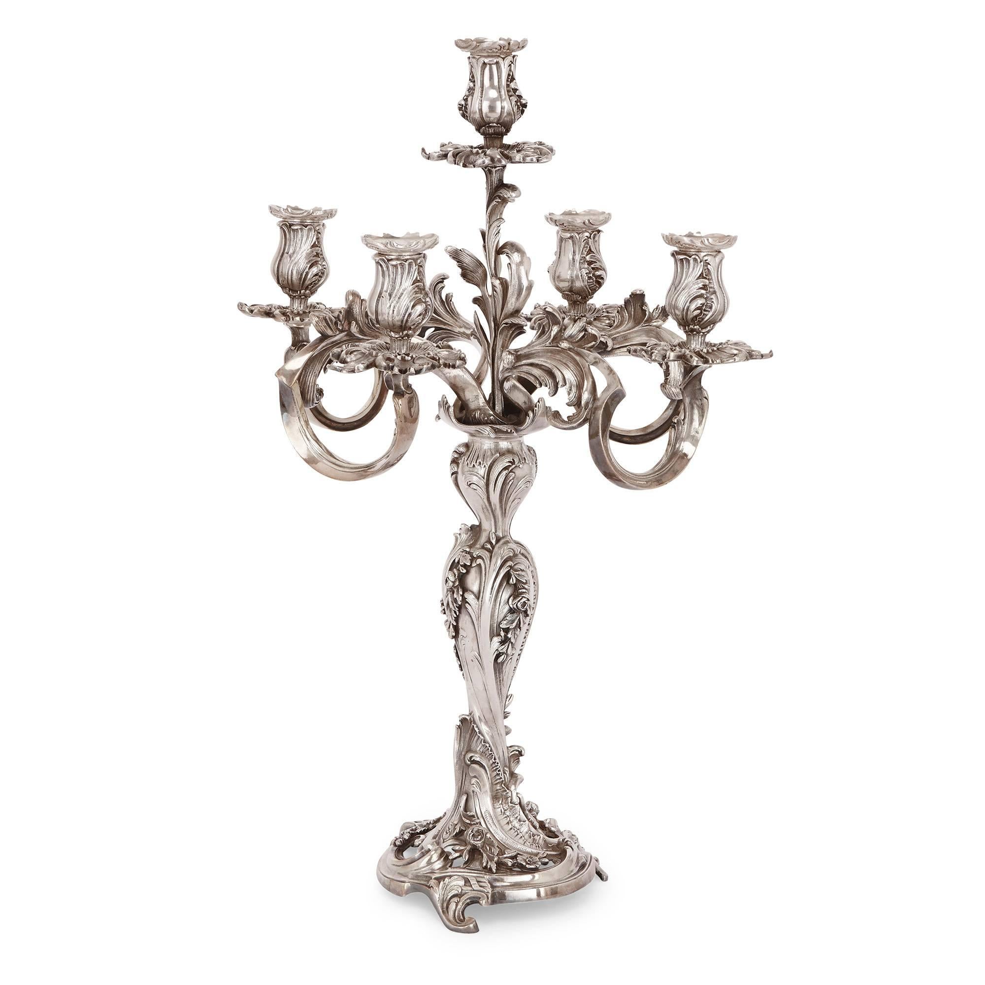 This pair of French antique candelabra are cast entirely in fine, silvered bronze in the Rococo style. They each stand on a circular base with curled feet and floral ornamentation, leading to a bulbous central column intricately worked with stylized