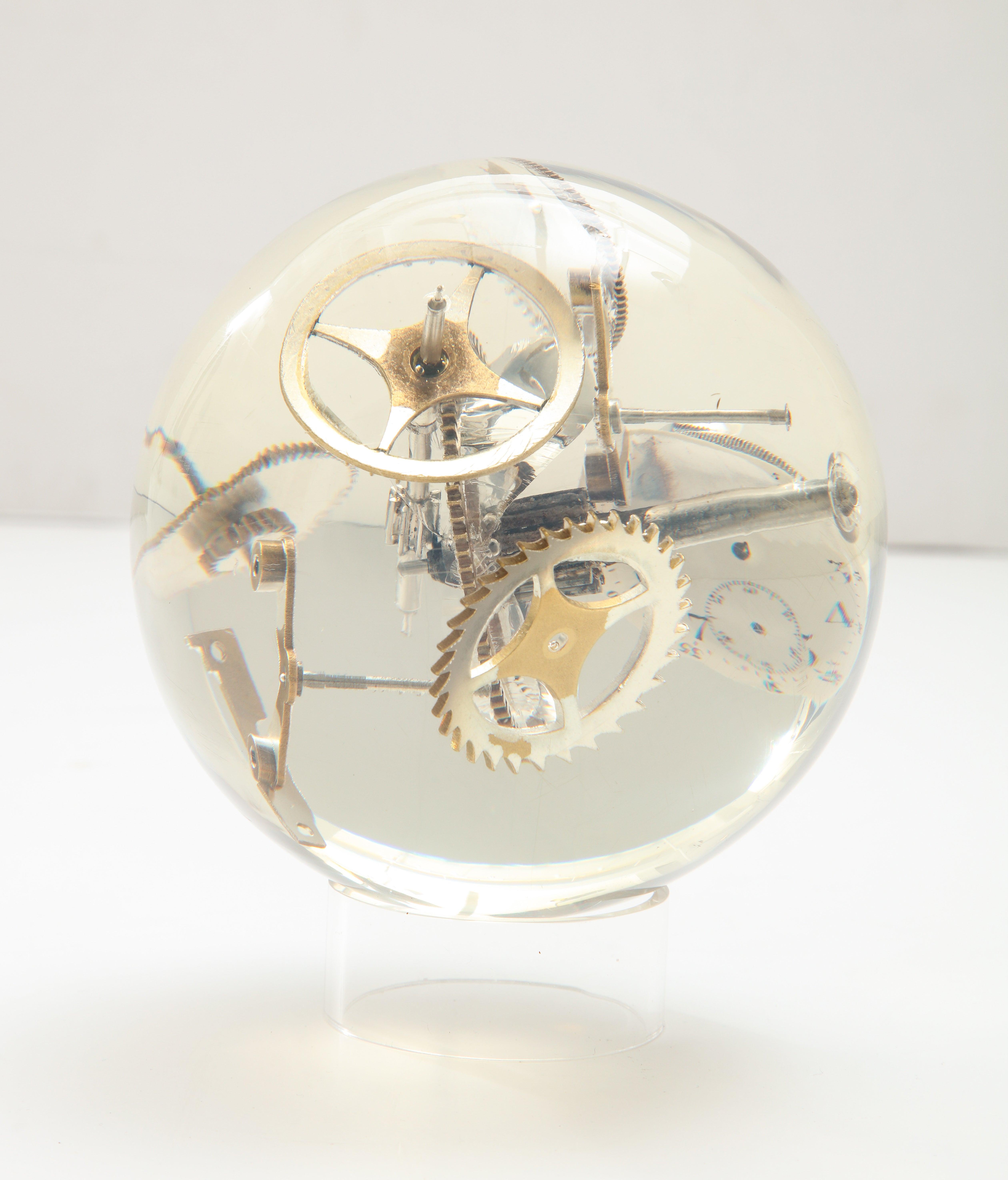 Resin sphere with exploded watch parts. Small scale chunky cast acrylic table sculpture with incased watch elements, including gears and a clock face. Sold with circular clear acrylic 2 inch stand.