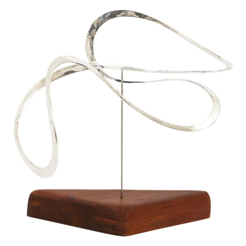 Russell Secrest sculpture, abstract, sterling silver, teak, signed. Kinetic sterling silver sculpture by modernist jewelry designer, Russell Secrest (1935-2010). The sculpture rotates on a polished steel rod which is sunk into a teak triangular