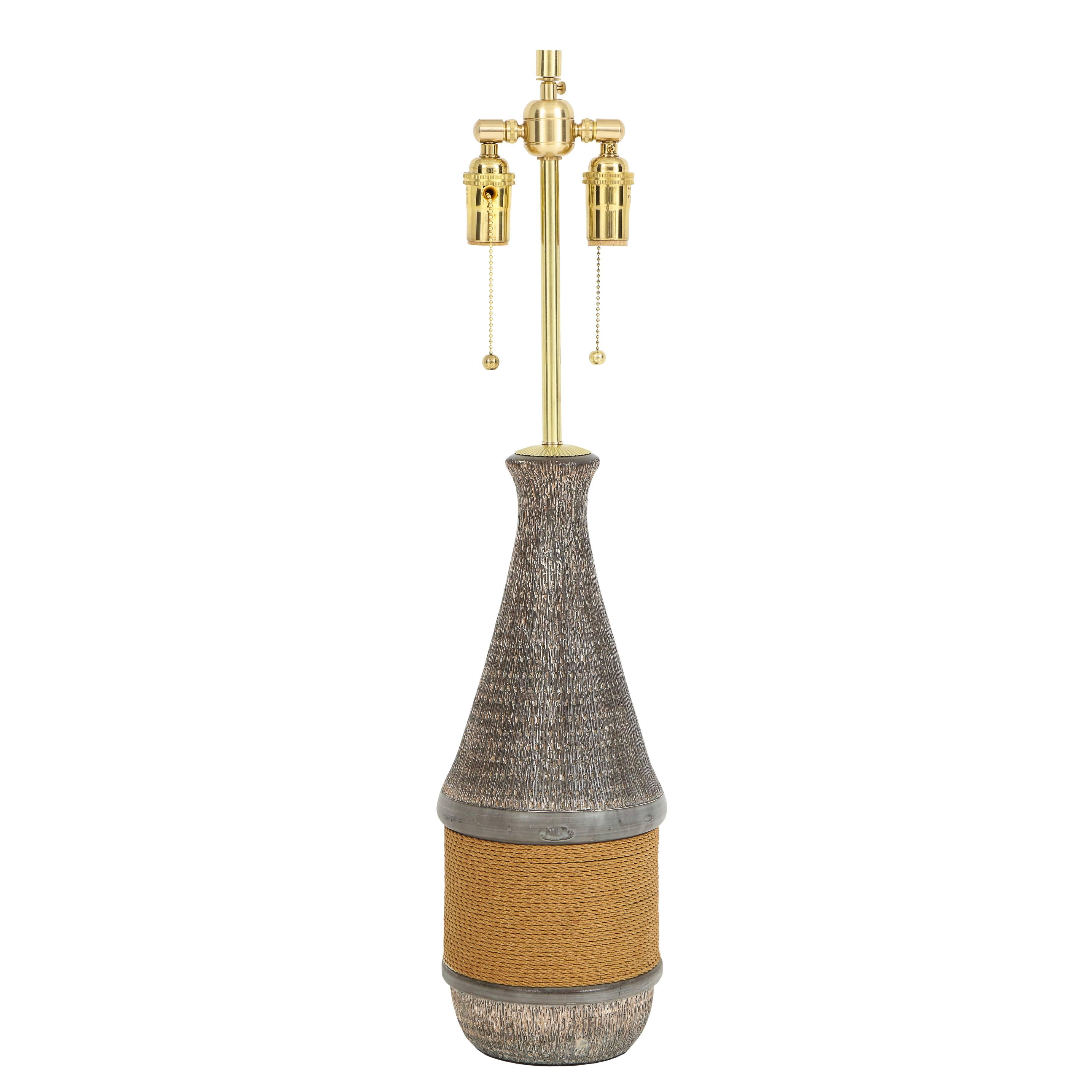 Aldo Londi Bitossi lamp, ceramic, rope, signed. Tall bottle form lamp with dark eggplant color glaze with a coarse impressed pattern. The belly of the lamp is wrapped in rope. Ceramic body measures: 17.75 inches. Signed on the underside: C 102/45,