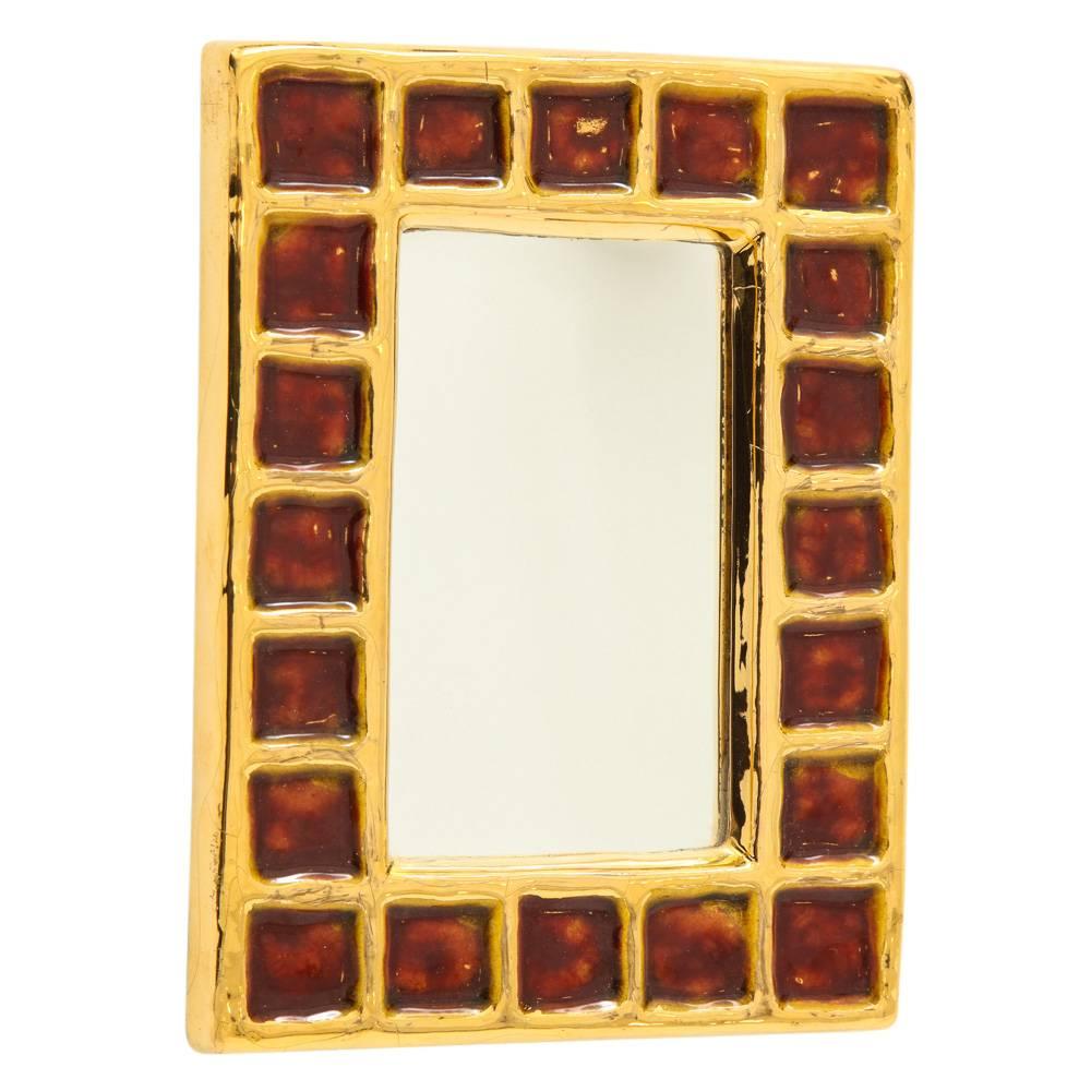 Francois Lembo mirror, ceramic, gold and red, signed. Small scale gold glazed mirror, decorated with a pattern of dark red (blood or ruby) squares. Signed Lembo with incised signature on the back. Crazing to the gold glaze frame. Embedded wire on