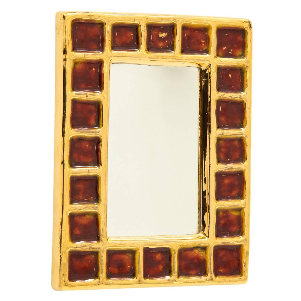Miroir François Lembo, céramique, or et rouge, signé. Miroir de petite taille à glaçure dorée, décoré d'un motif de carrés rouge foncé (sang ou rubis). Signé Lembo avec signature incisée au dos. Craquelures sur le cadre en glaçure dorée. Fil de fer