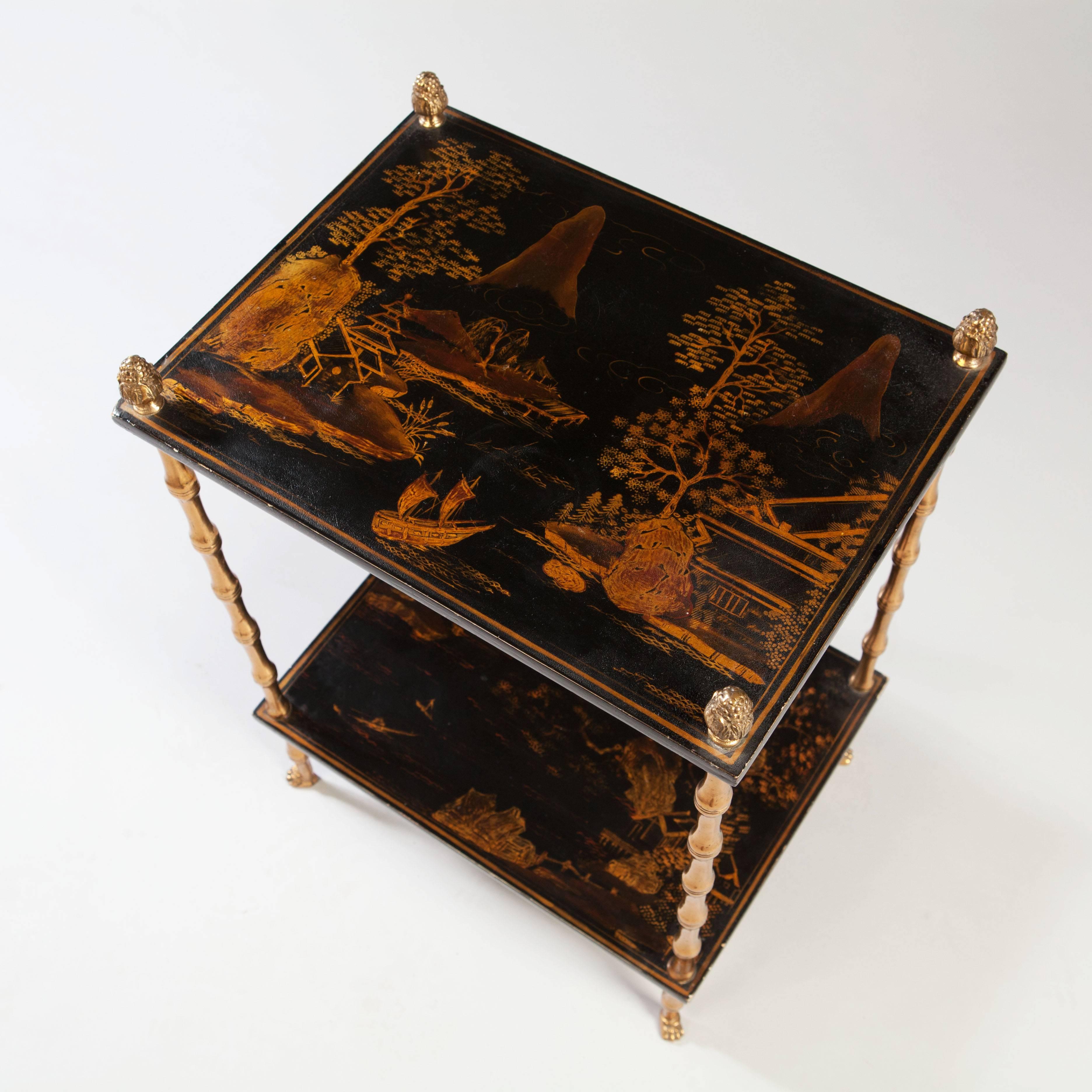 A fine Chinoiserie lacquer two tier occasional table, decorated with mountainous landscapes and Chinese pergolas, supported on faux bamboo legs atop paw feet.