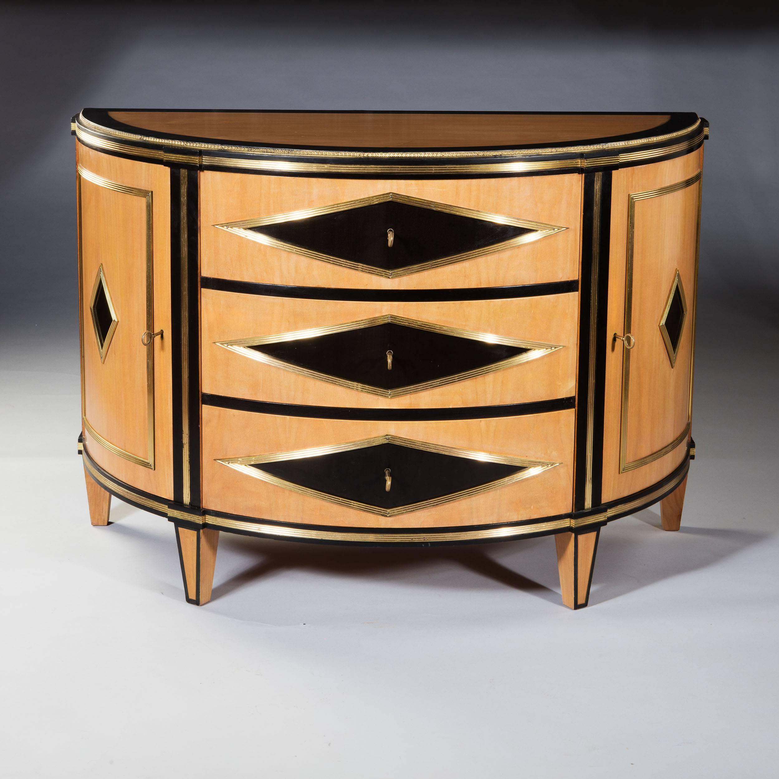 A fine early 20th century maple and ebonized demilune commode with three drawers and side cupboards, all supported on toupie feet.