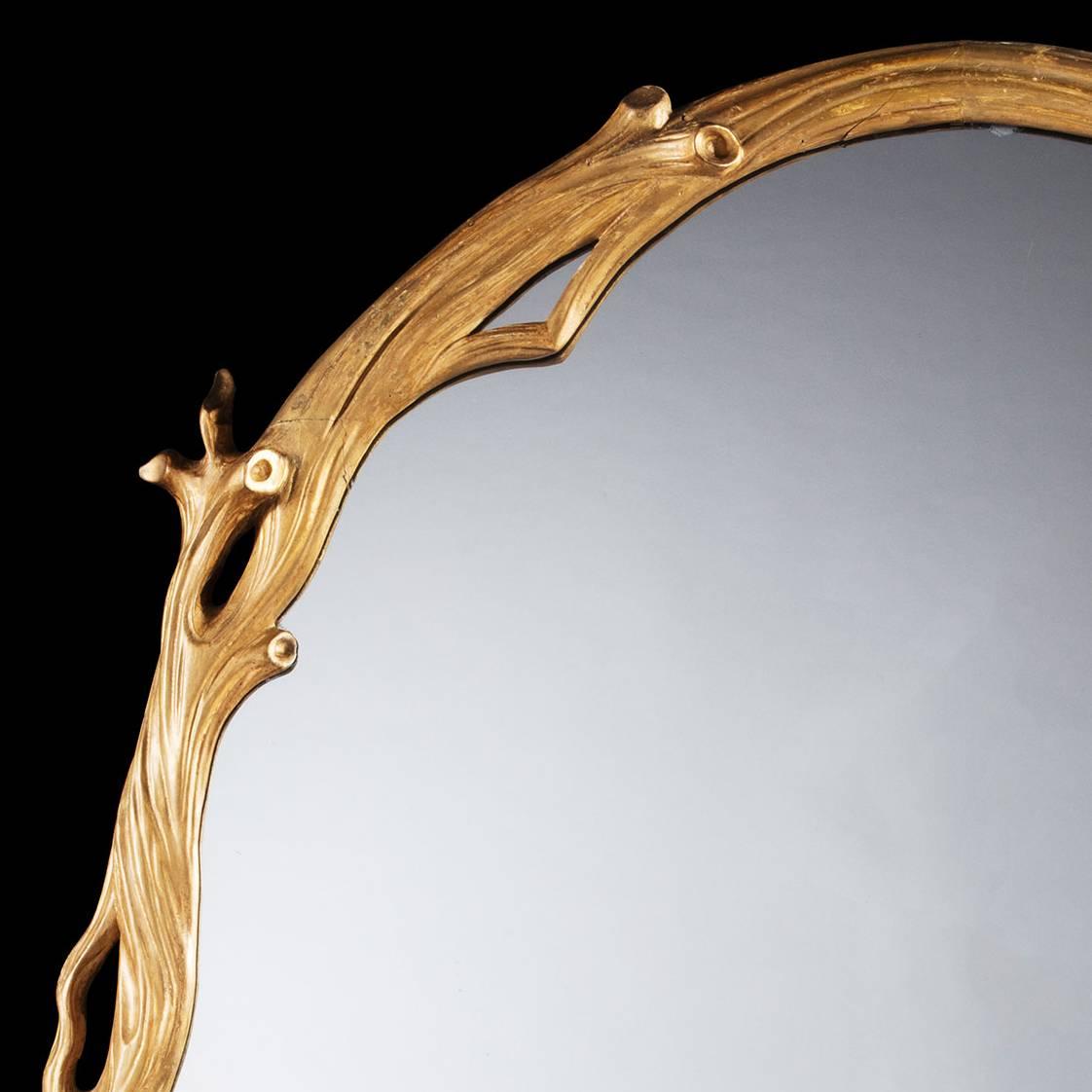 A large oval giltwood mirror with carved frame in the form of interlocking tree branches.