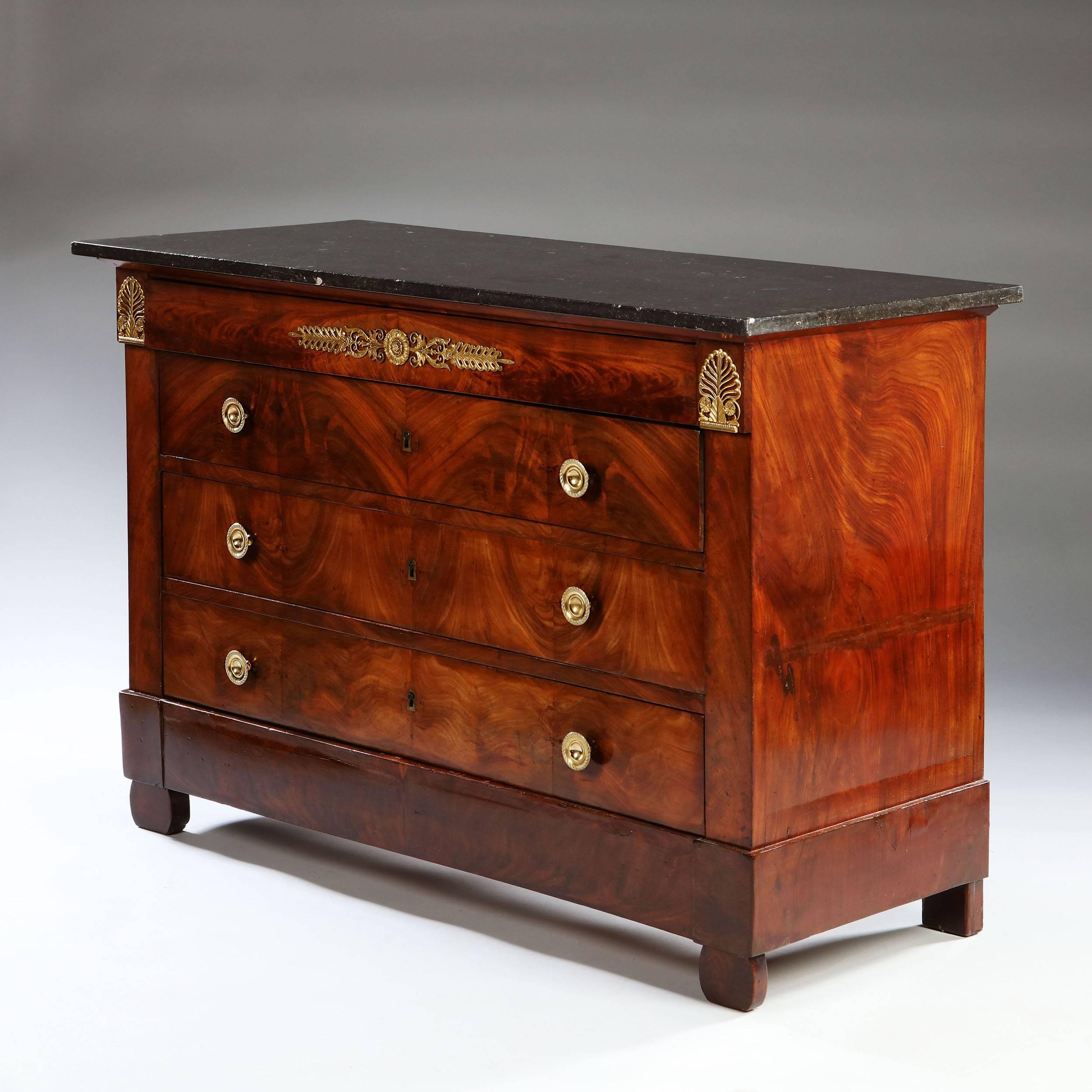 An early 19th century Empire mahogany commode, with book matched flame veneers to the front, opening with four long drawers, with original finely chased ormolu mounts, retaining the original grey marble top, and all supported on four bracket feet.