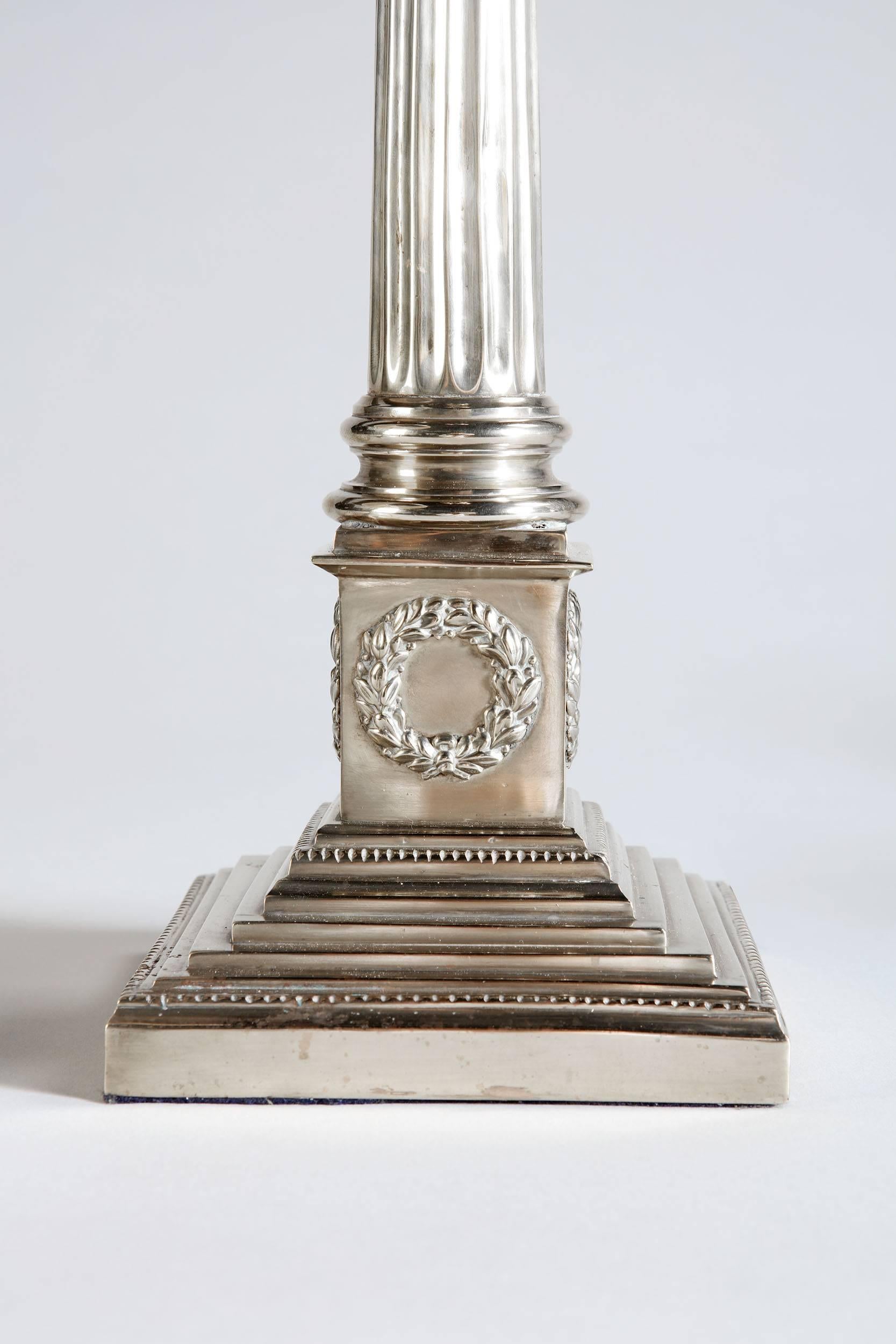 A pair of silver column lamps with fluted columns and Corinthian capitals, all supported on square bases.