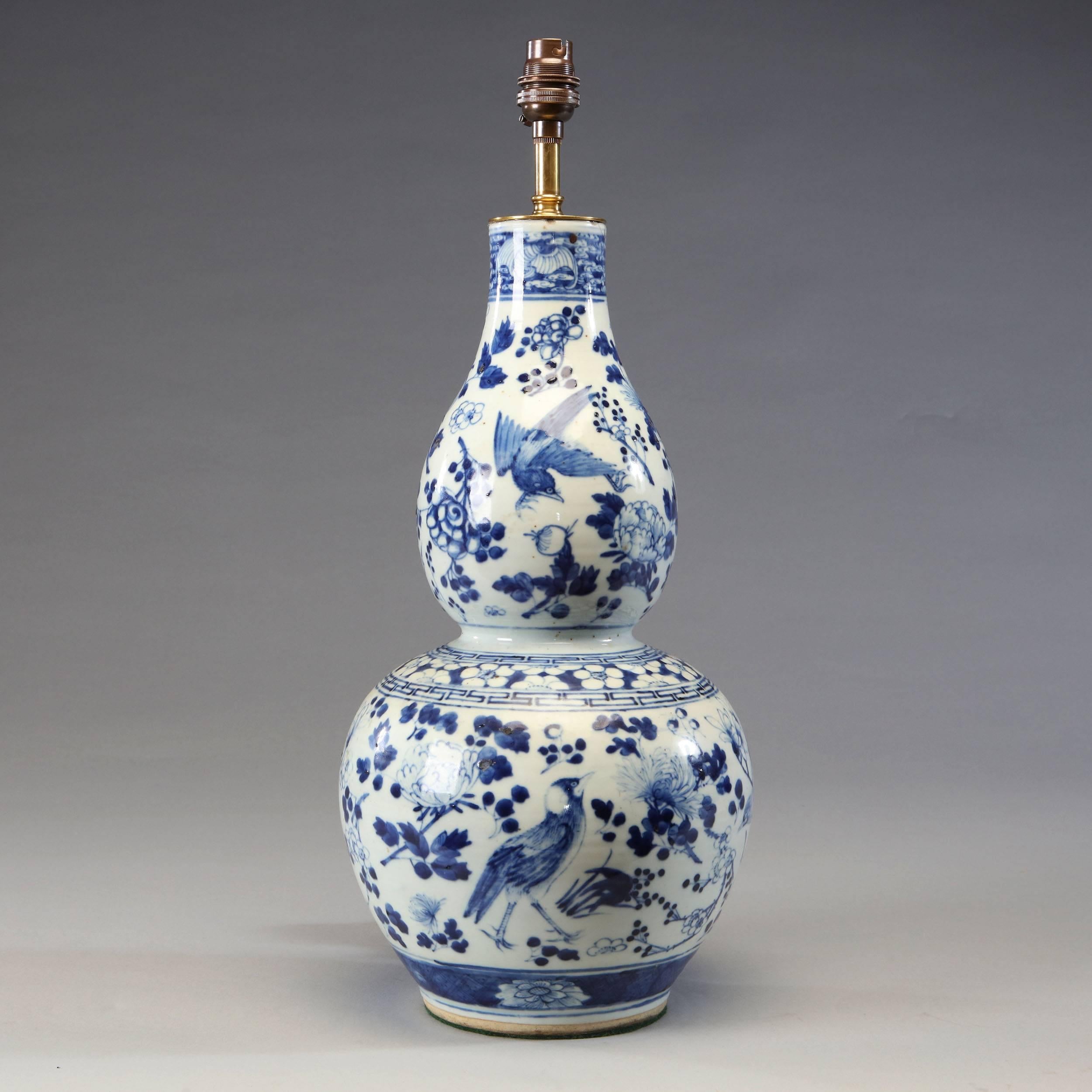 A fine pair of 19th century Chinese blue and white vases of double gourd form, decorated with tropical birds and flora, now converted as lamps.