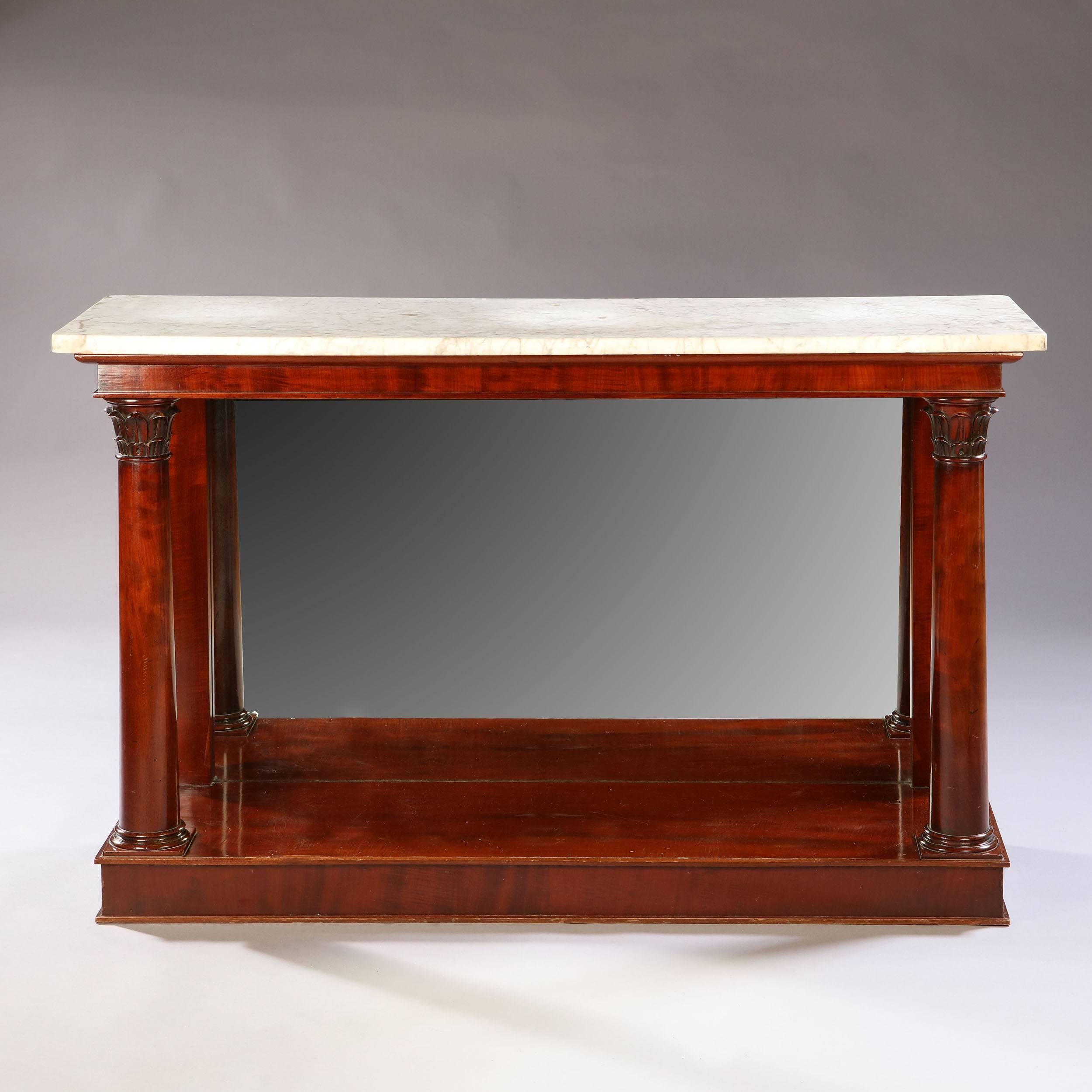 An early 19th century Empire period mahogany console table, with original marble top and a mirror plate to the back, with carved Corinthian capitals to the top of the uprights.