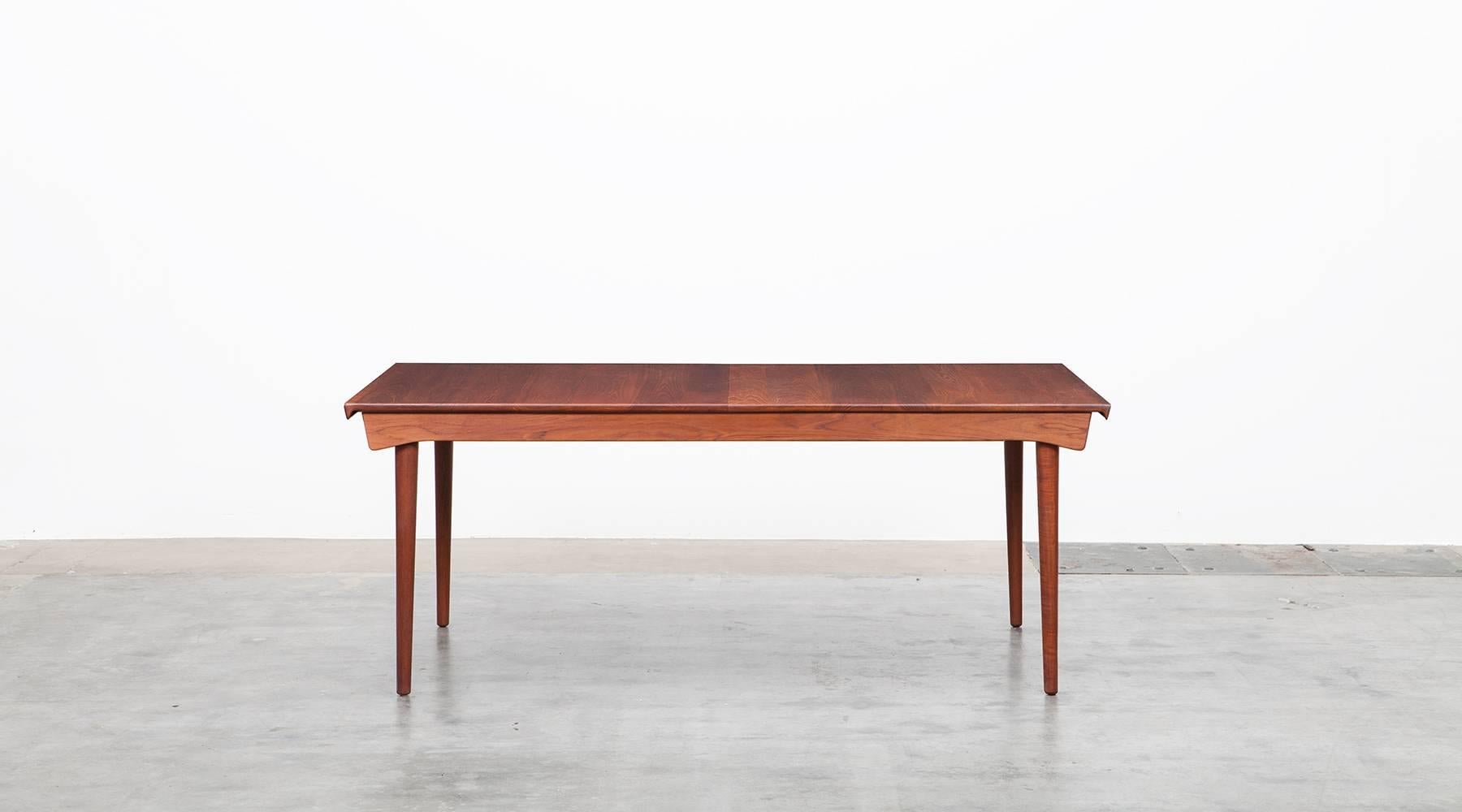 This extendable table designed by Finn Juhl is made of solid teak and combines elegant forms with practical functions. Two teak leafs stow beneath the table. The sculptural lips at both ends of the table are handles to open and close it. Measure: