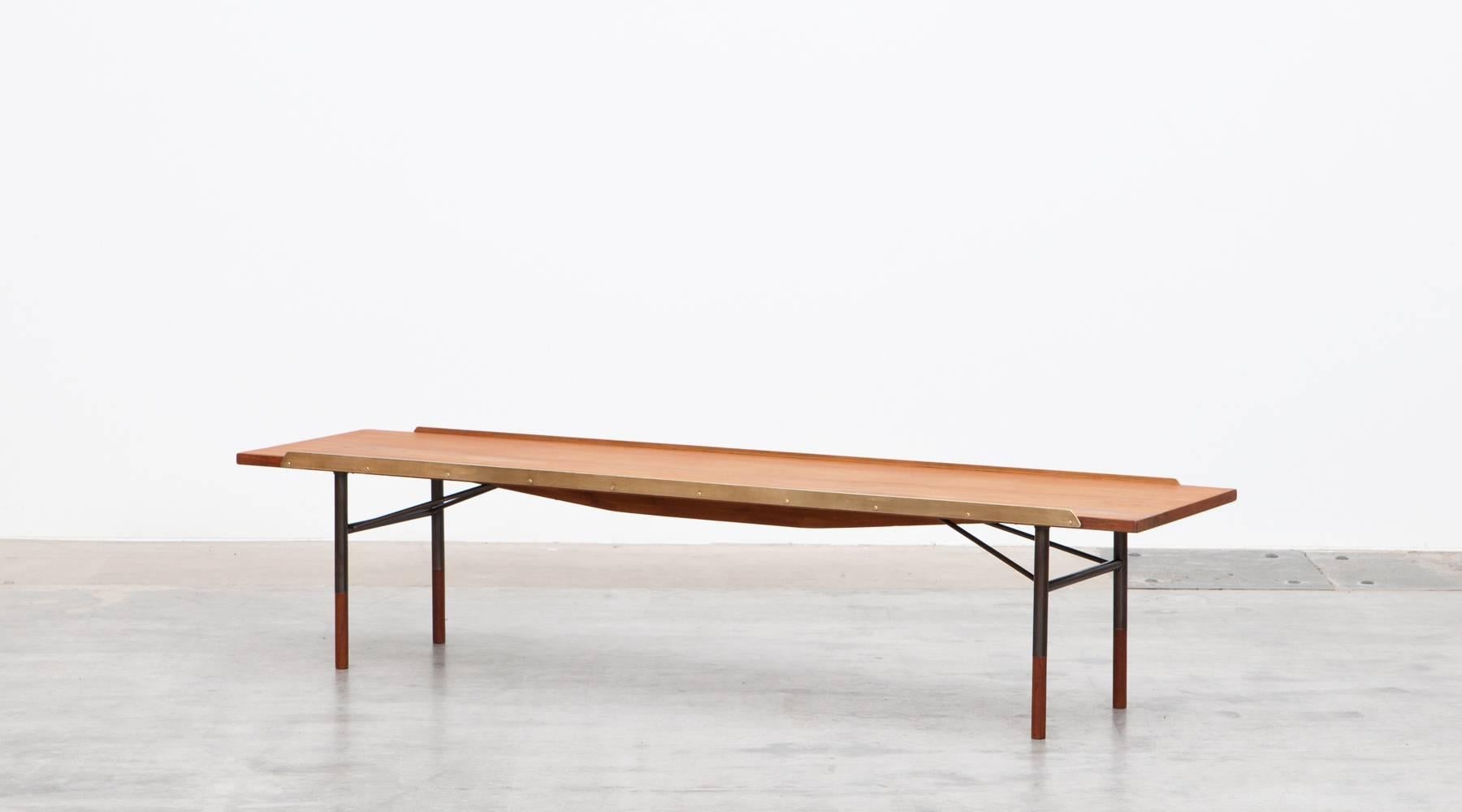 This design was conceived by Finn Juhl to be used as a bench and/or coffee table. The top surface is flanked by two solid brass strips that would have kept cushions in place but also guard against items on the surface falling off. The legs are
