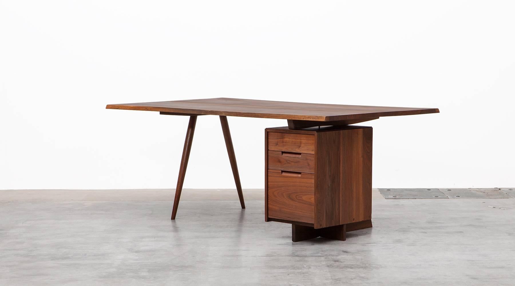 This Classic desk by George Nakashima has a beautifully figured American black walnut slab top with an organic and subtle free-form edge. On one side, its features storage cases with one large and two small drawers and on the other two elegant