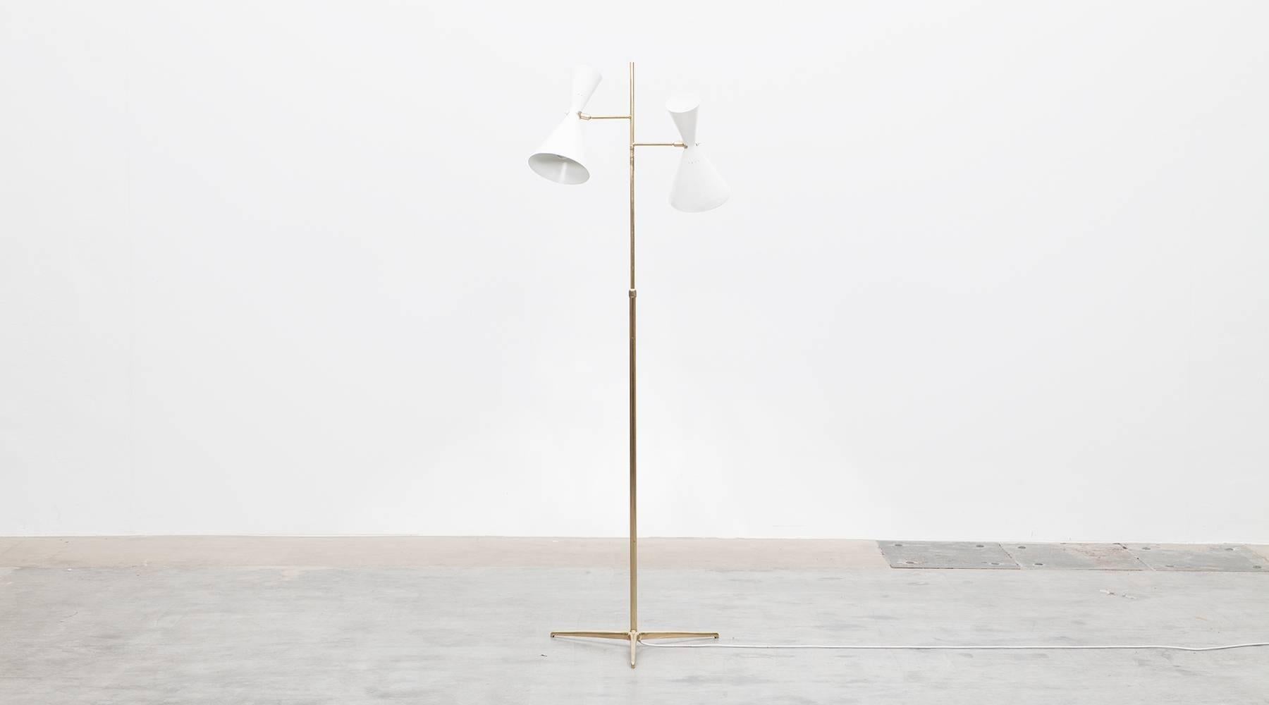 Beautiful floor lamp with two perforated, white lacquered aluminum shades mounted on a brass stem ended elegantly on three feet. Great details. Manufactured by Swiss Baumann Kölliker AG.