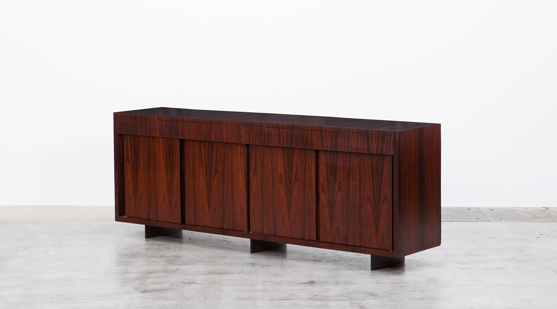 This four-door sideboard is very rare to find and designed by famous Brazilian Joaquim Tenreiro. The Sideboard comes in wood and contains underneath the top four drawers which externally on the first view are not visible. Manufactured by Tenreiro