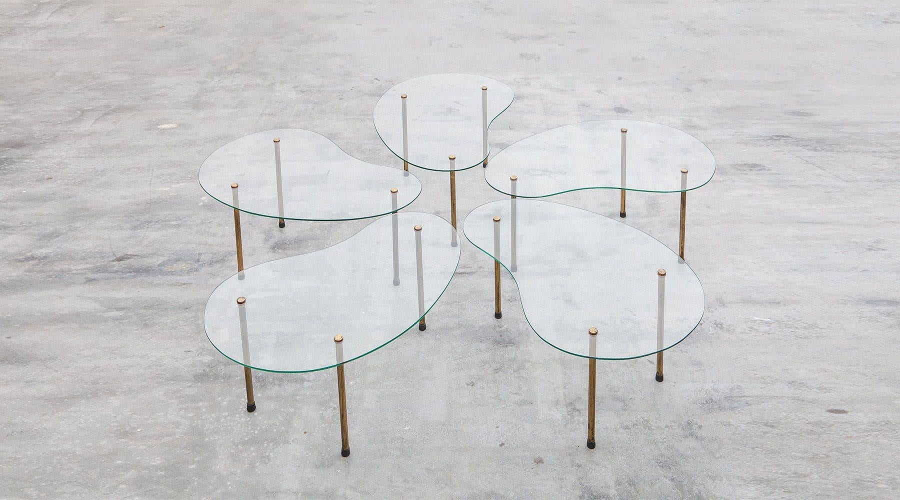 Beautiful set of very functional side tables attributed to the design of Peter Hvidt. Five identical tables, each with a crescent shape in glass and three brass legs, can be configured to almost any form you like. The brass legs have their original