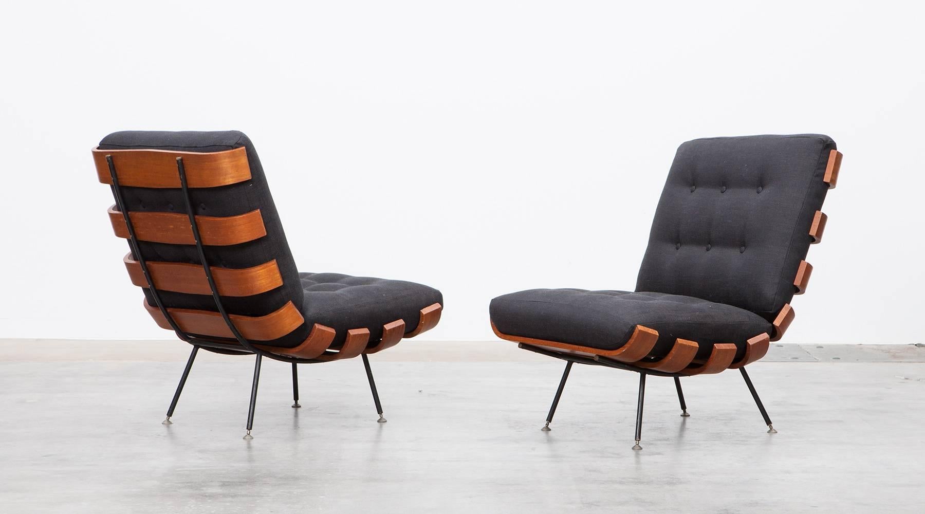 Wonderful Brazilian lounge chairs designed by Martin Eisler and Carlo Hauner. This pair has been produced in teak and plywood slats bent elegant to the ends and stands on a black lacquered metal frame with brass feet. The cushions are recently newly