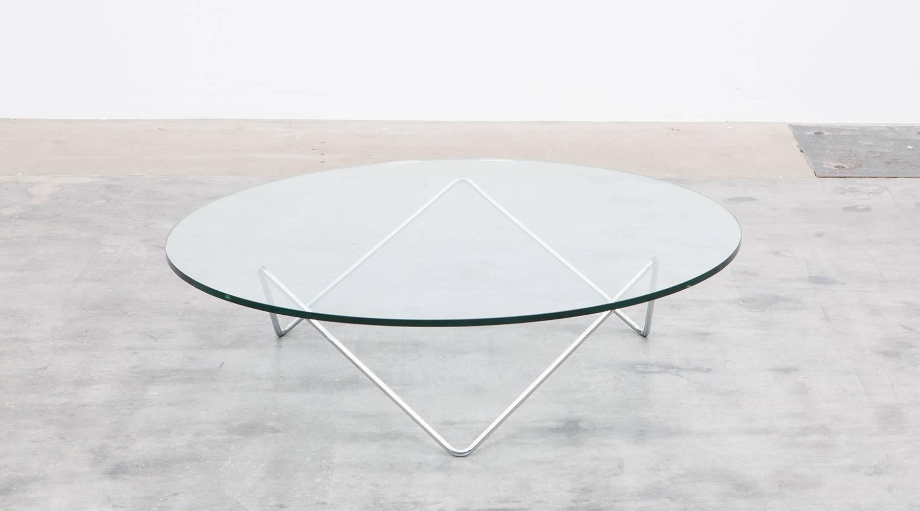 The coffee table with a round glass top on metal pipe chromium plated base is designed by German architect Herbert Hirche. The unusually wide perfectly preserved glass plate is supported by geometrically balanced metal feet. Manufactured by