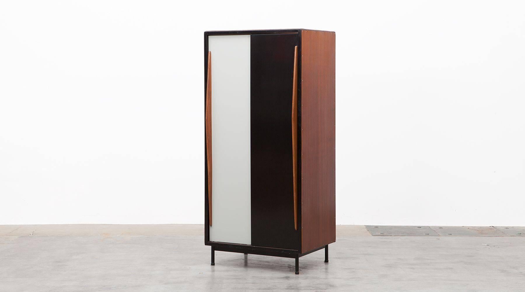This standing cabinet with lacquered metal doors in black and light grey and wooden door handles, slides from left and right. Contains wardrobe on one side and two shelfs on the other side. Nice early example of Industrial Design from the Belgium
