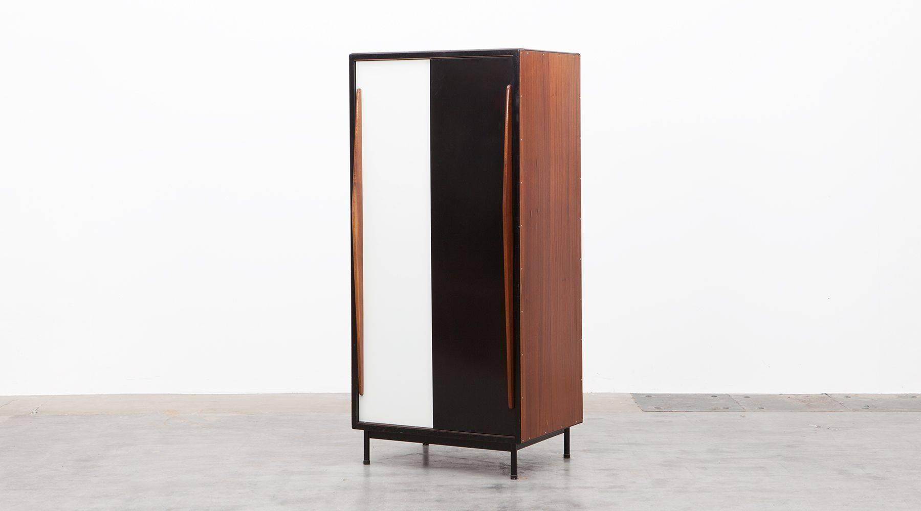 This standing cabinet with lacquered metal doors in black and white and wooden door handles, slides from left and right. Contains wardrobe on one side and two shelf’s on the other side. Nice early example of Industrial Design from the Belgium