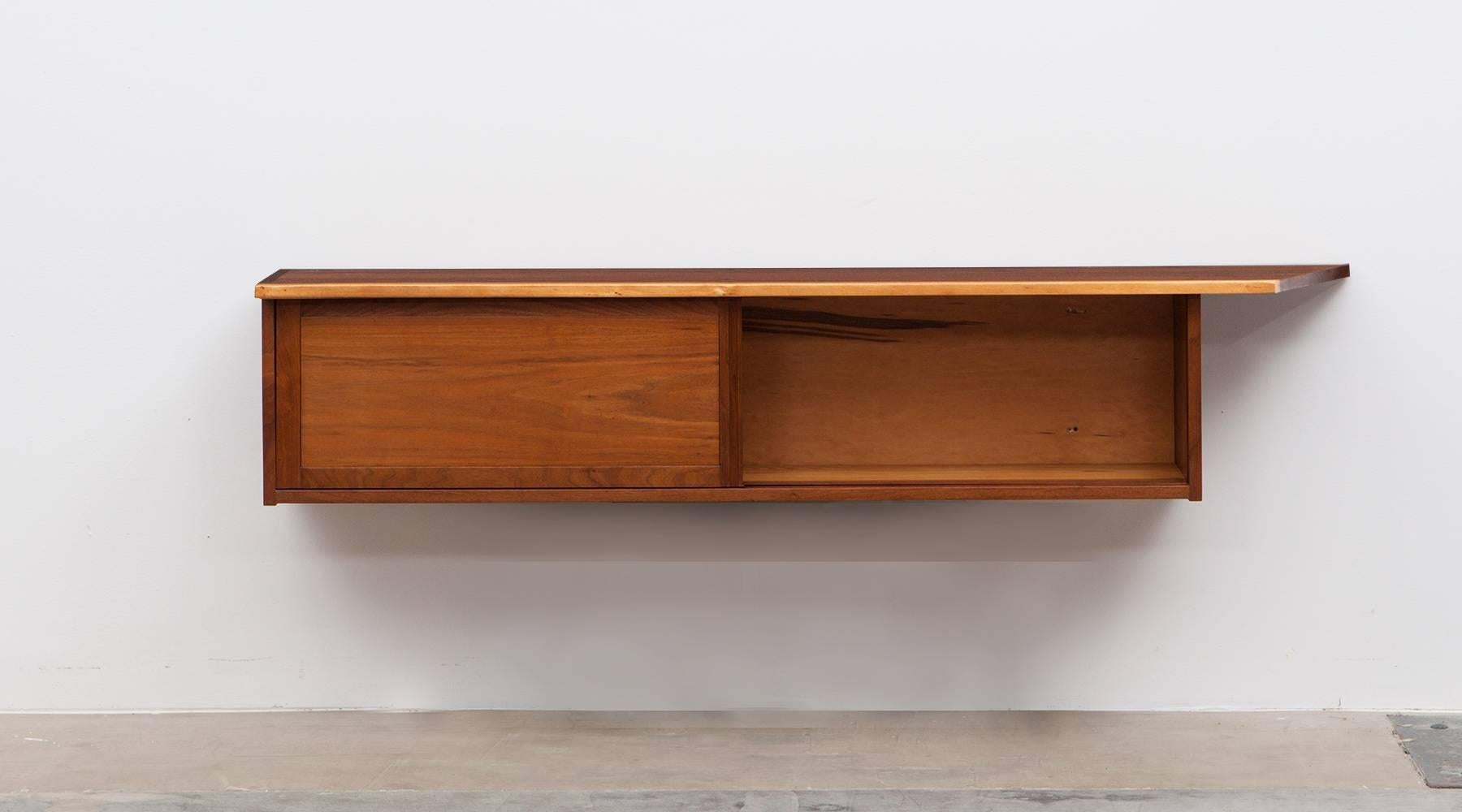 This handcrafted and wall-mounted sideboard by George Nakashima has a beautifully figured American black walnut slab top with an organic and subtle free-form edge. Comes with two sliding doors, containing three shelves. Manufactured by George